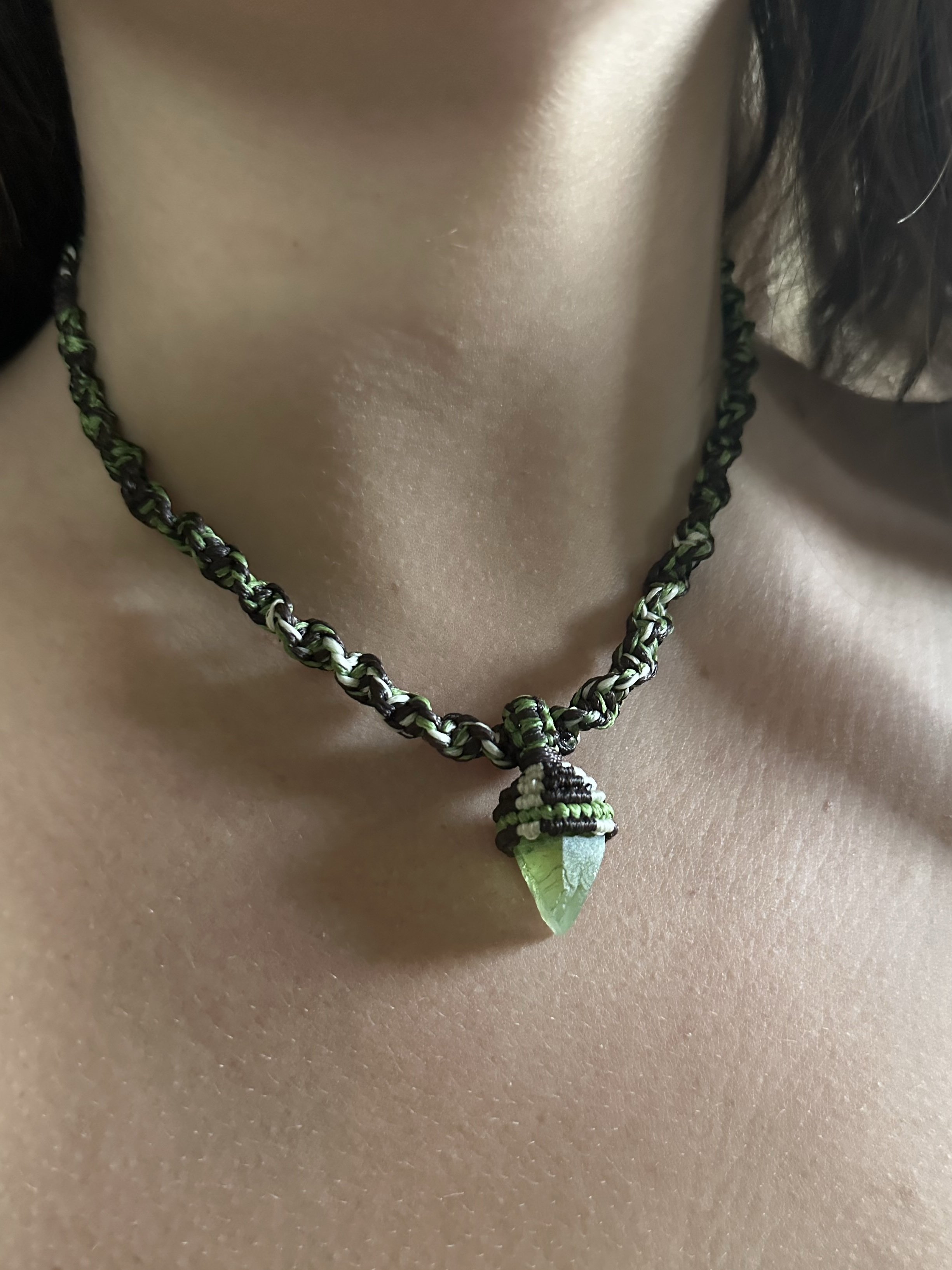 A close-up of a necklace with a green, leaf-shaped pendant worn around a person's neck.