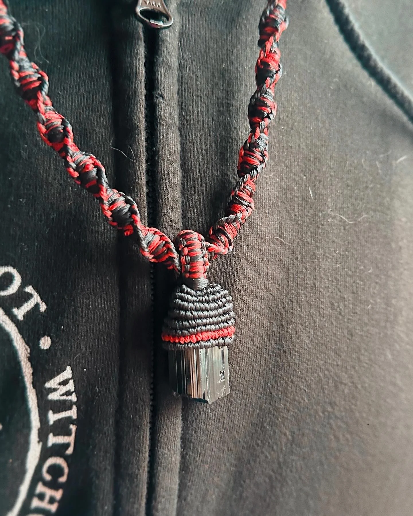 Close-up of a paracord-wrapped small object with a metallic tip, attached to a black fabric surface with partially visible white text.