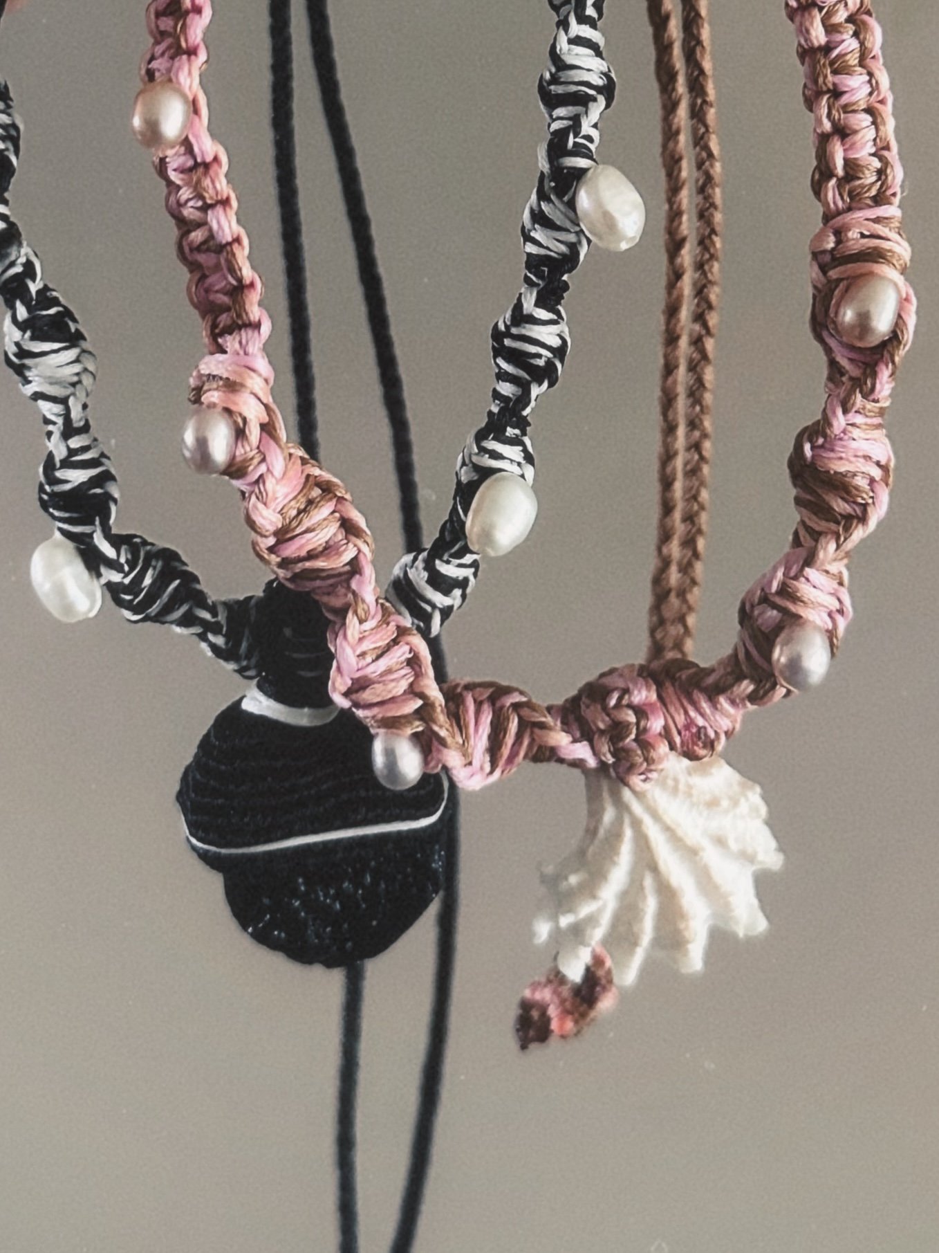 Close-up of handmade friendship bracelets with pearl beads, made from different types of thread, hanging against a neutral background.