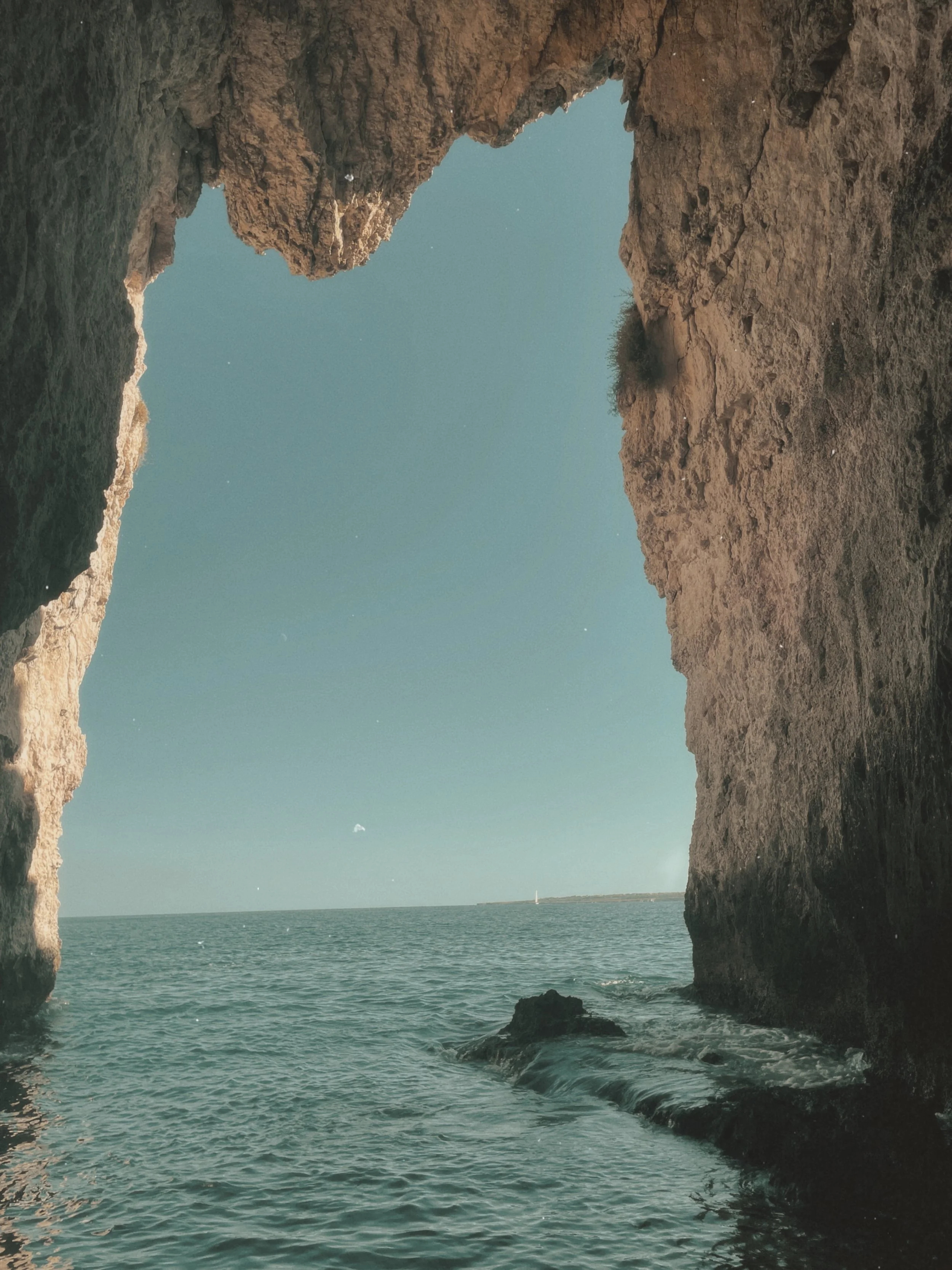 Cliffside view of the ocean with a natural rock arch framing the sky and horizon in the distance.