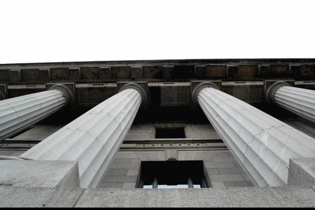View of four tall, white, classical columns supporting a building against a cloudy sky.