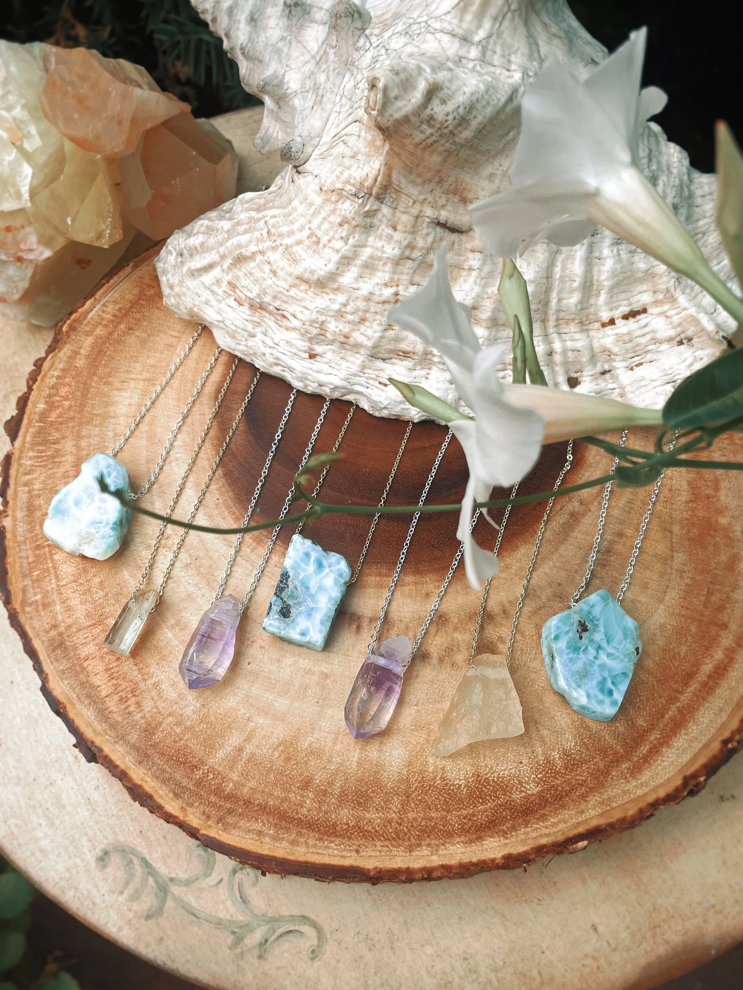 A collection of colorful gemstone necklaces displayed on a wooden slice with a decorative background.