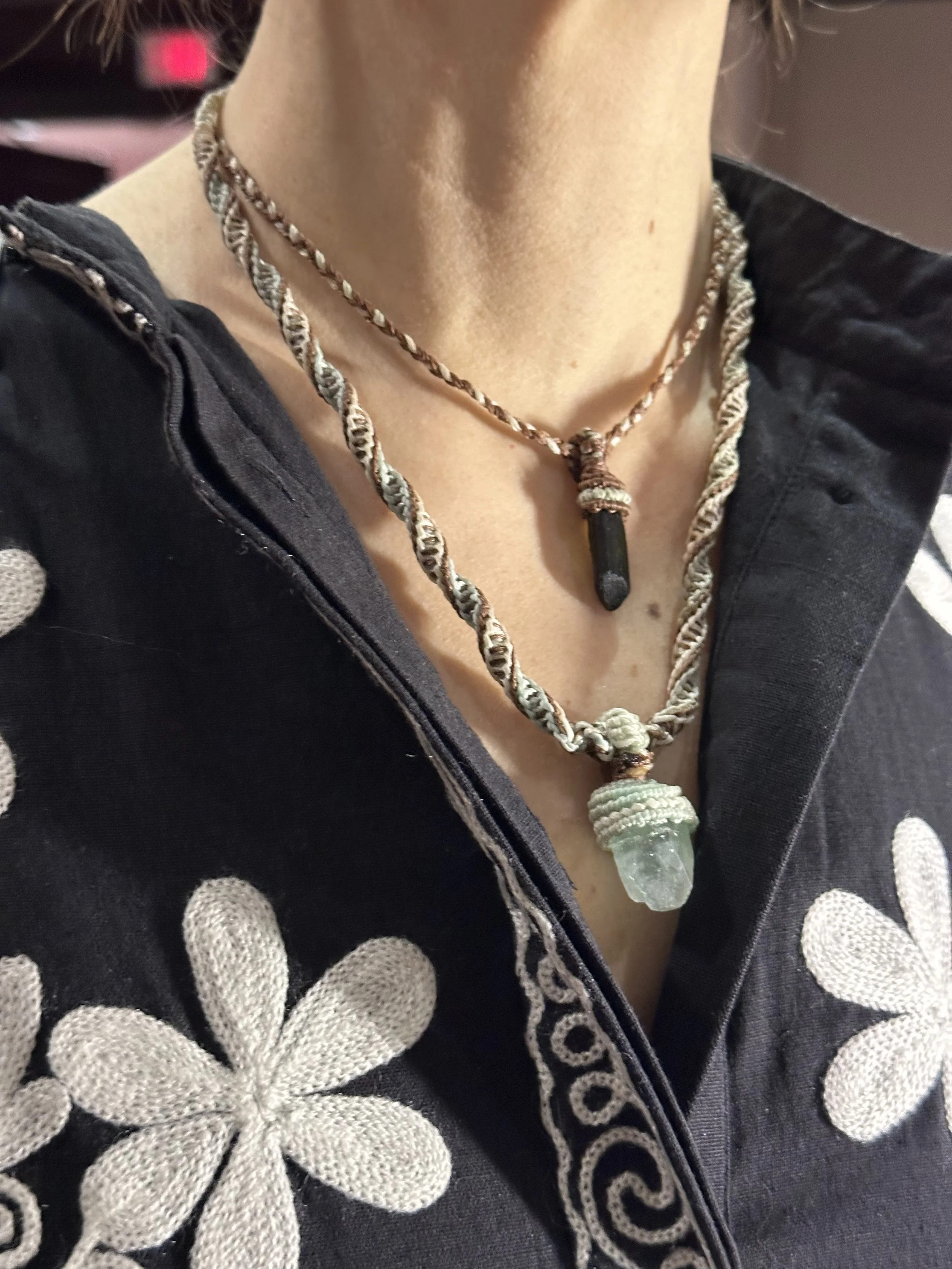Person wearing a black robe with white polka dots and a beaded necklace with a large, light green crystal pendant.