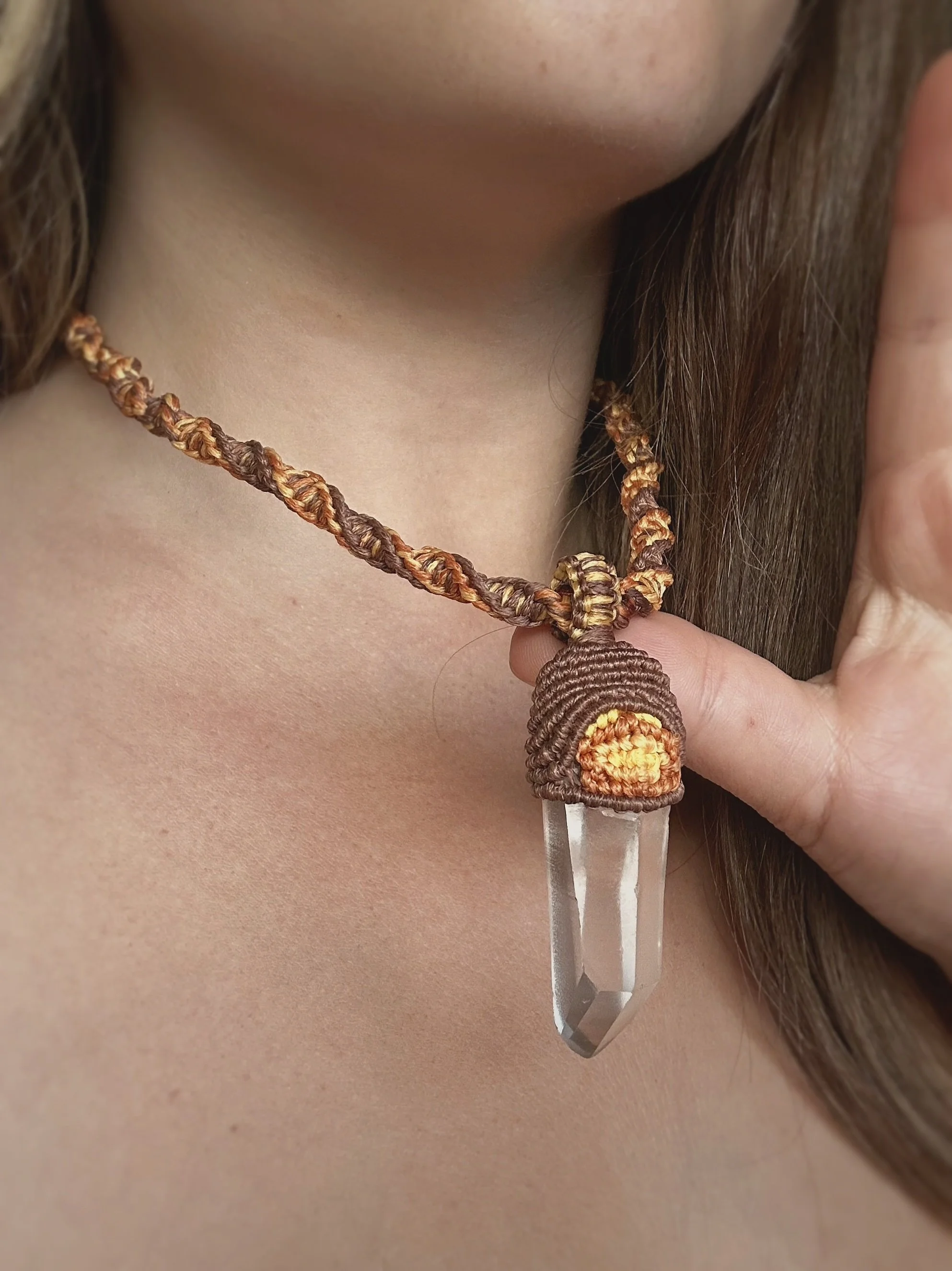 Close-up of a person with a glucometer used for blood sugar testing, attached to a braided cord necklace with a decorative element, and having long brown hair.
