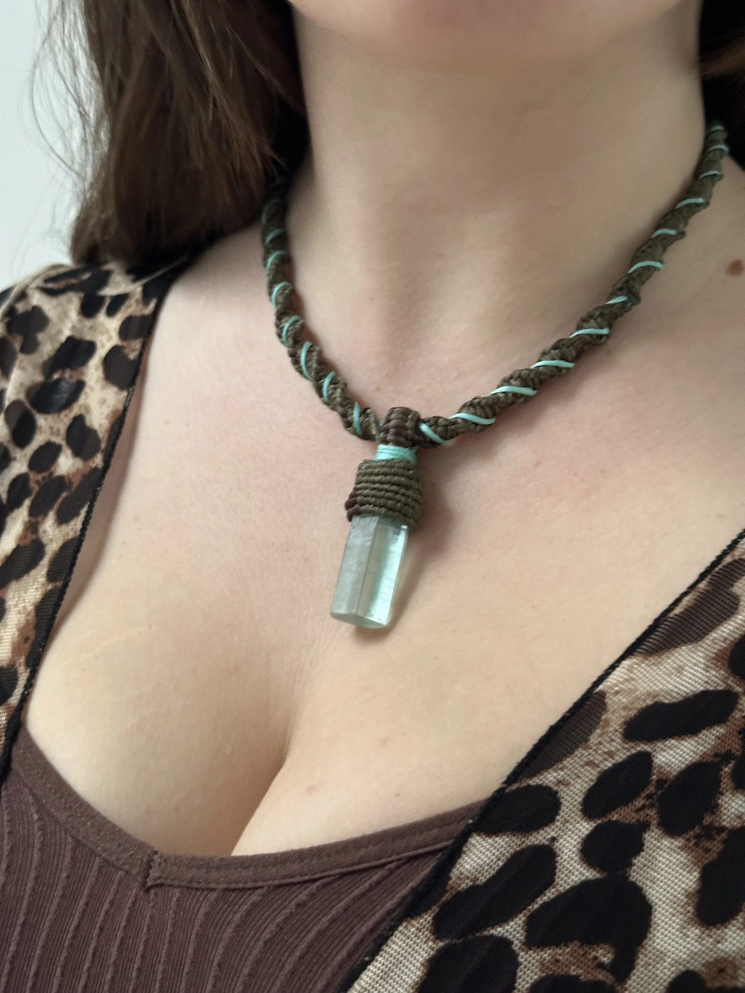 A person wearing a leopard print top with a necklace that has a green stone pendant.