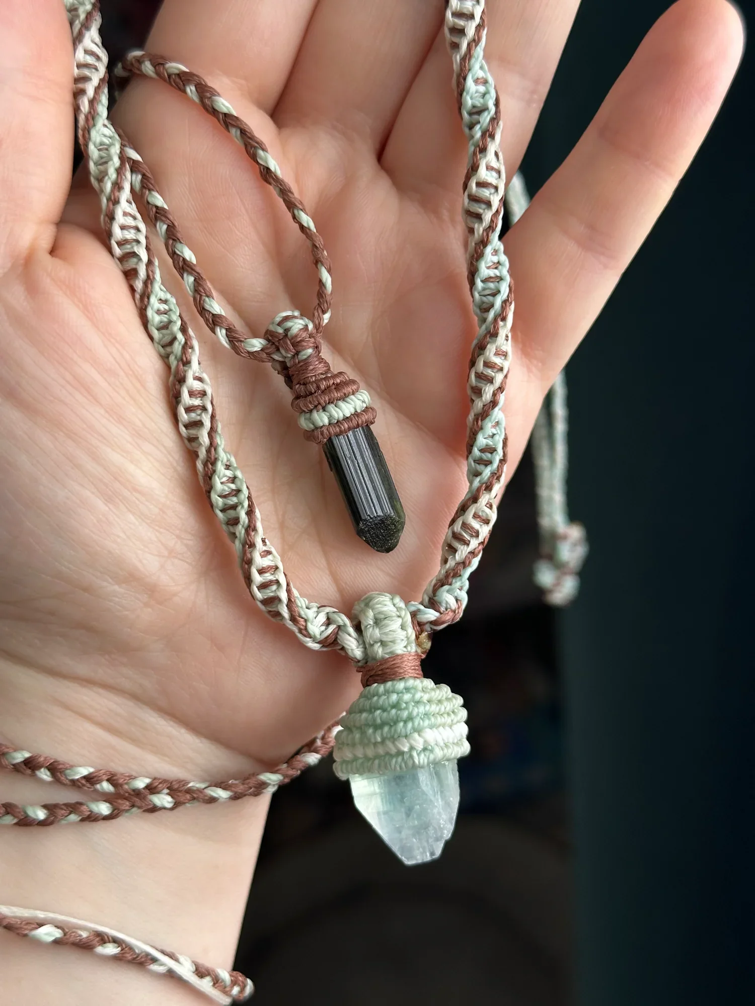 Hand holding a pendant necklace with a clear crystal point and woven cord.