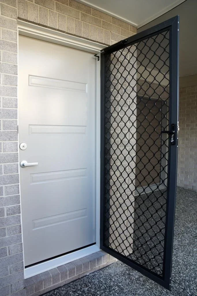 A white front door with a security screen door propped open, showing a brick exterior wall and concrete porch.