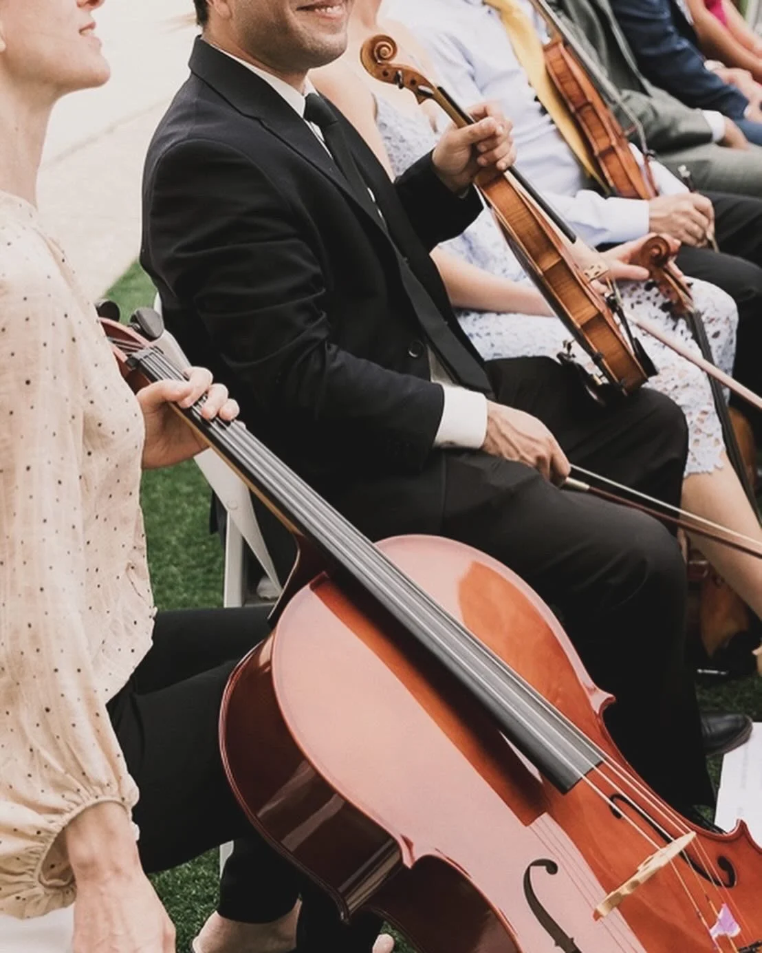 Musicians playing string instruments, including violins and cellos, in an outdoor setting.