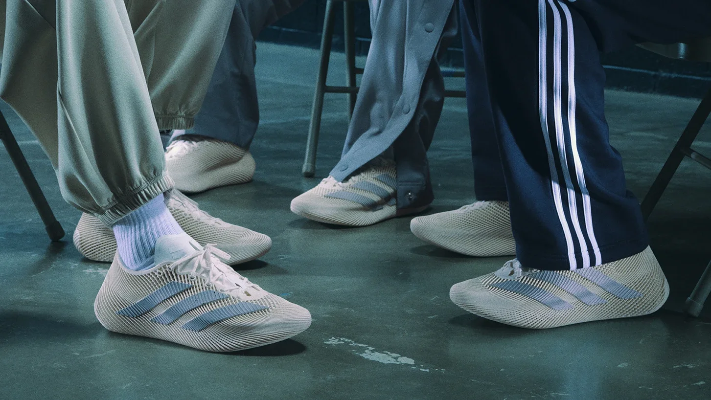 Several people sitting at a table wearing beige sneakers with blue stripes, light-colored socks, and sports pants or track pants.