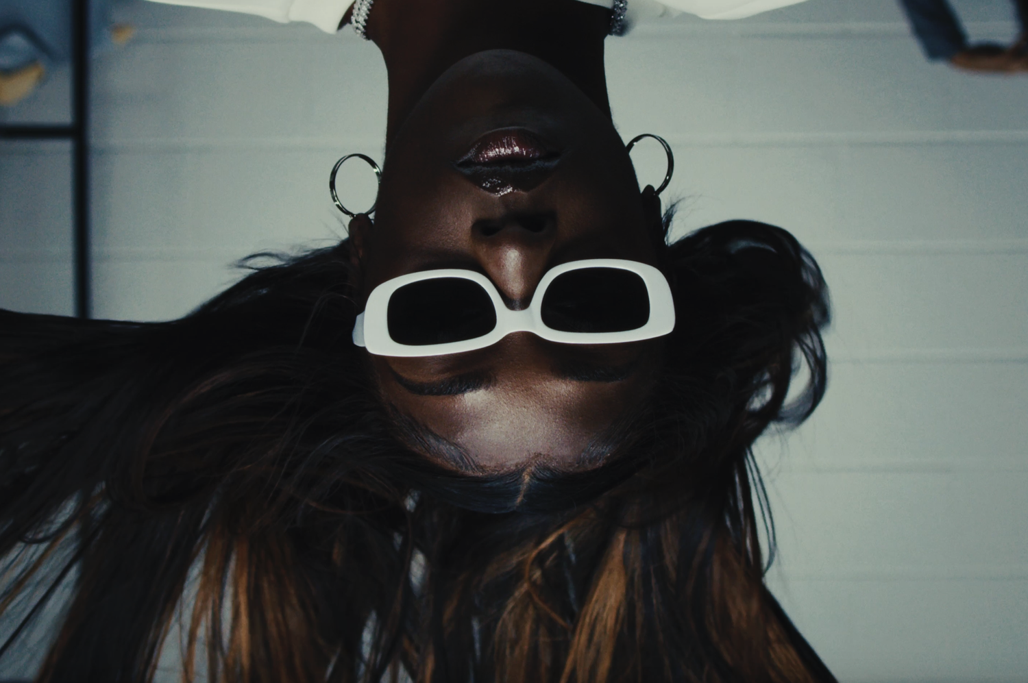 Upside-down photo of a woman with sunglasses, earrings, and long hair.