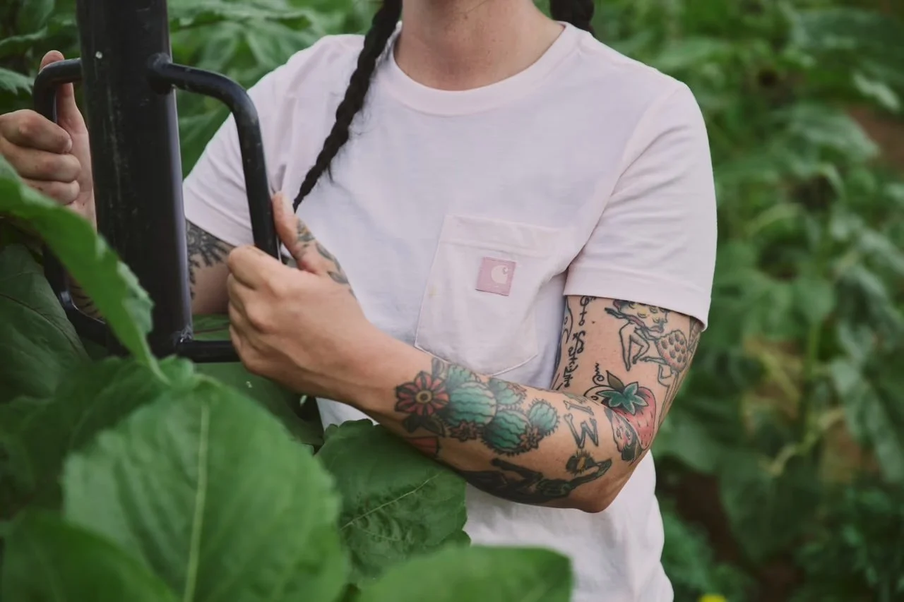 Person with tattoos on arms using gardening tool in a green garden or farm.