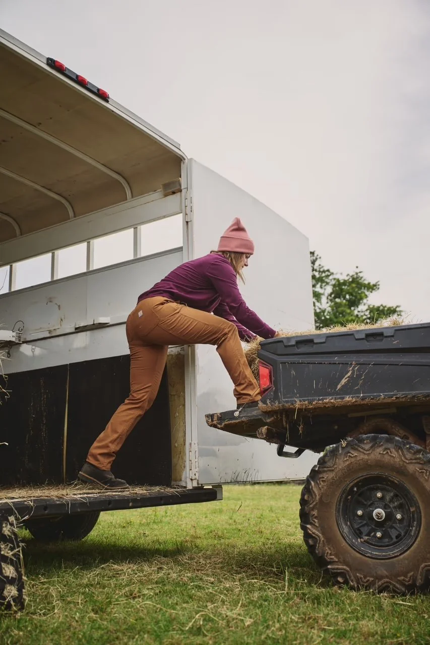 A person loading hay into the back of a horse trailer using a scoop on a farm or rural area.