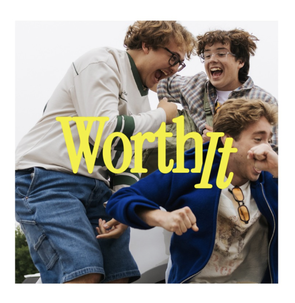 Group of four young men smiling and laughing together outdoors, with one of them playfully punching another in the arm. The word 'WorthIt' in bright yellow letters is overlaid on the image.
