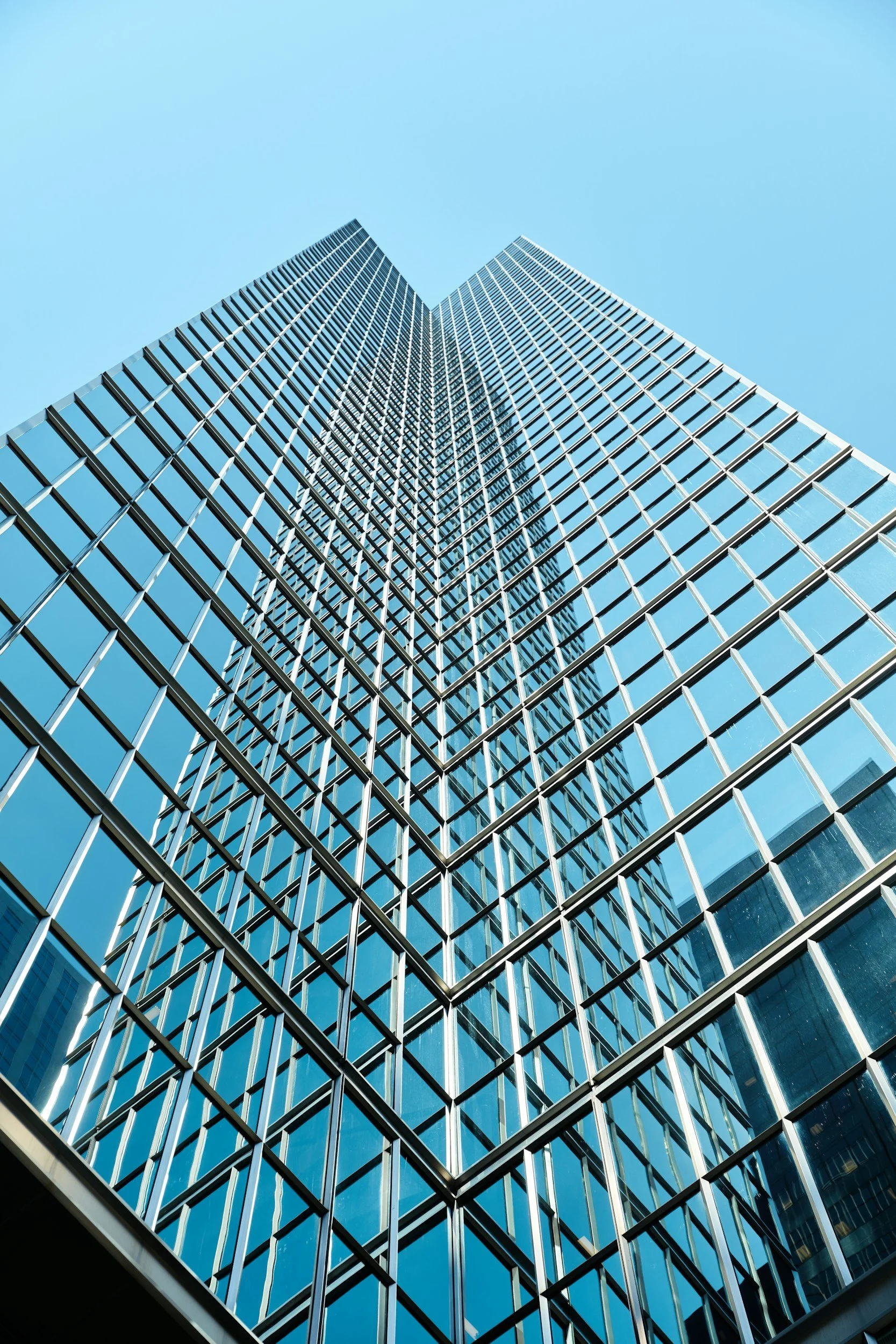 Glass office tower seen from below against a blue sky