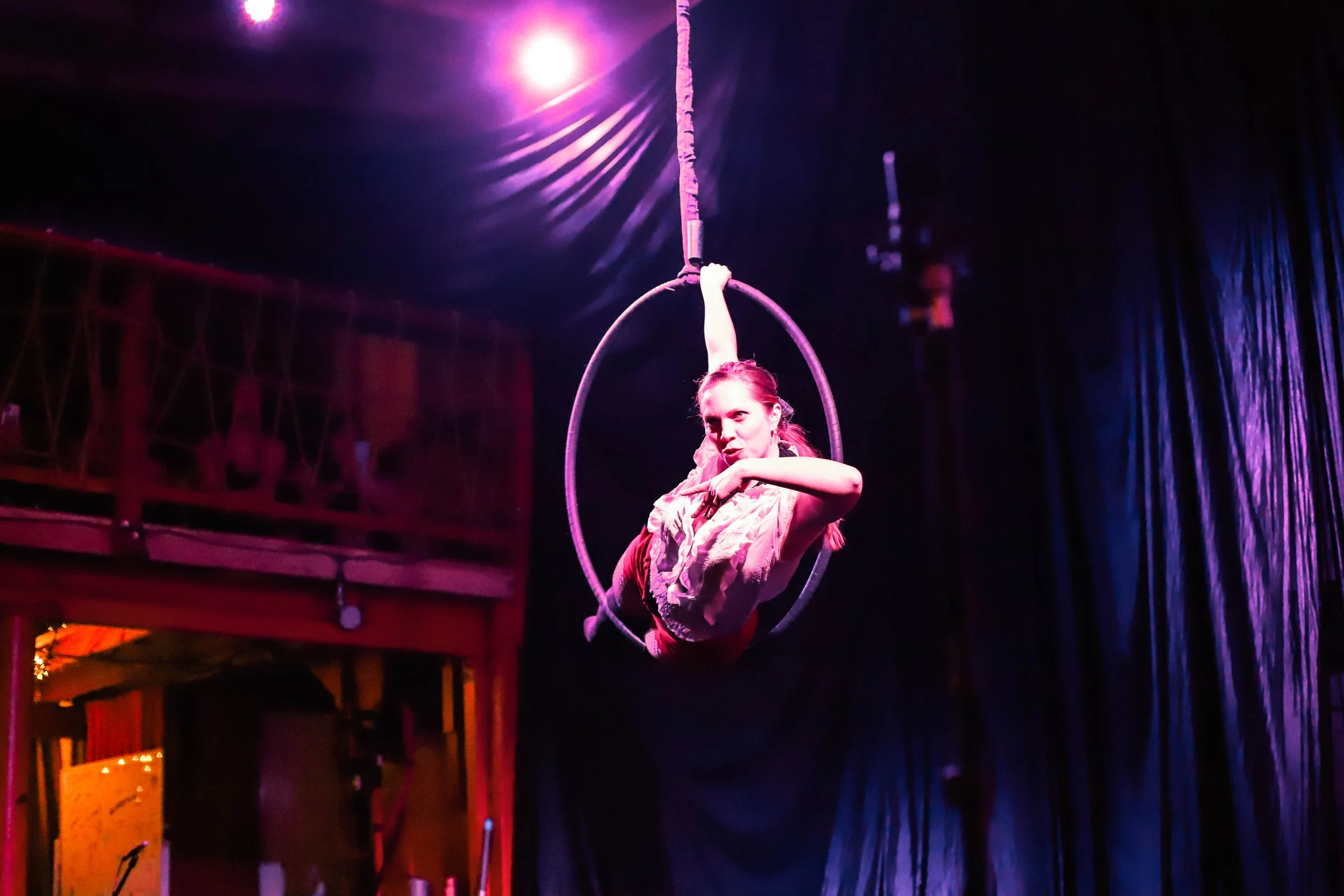 A circus performer on an aerial hoop, performing under colorful stage lights in a dark venue.