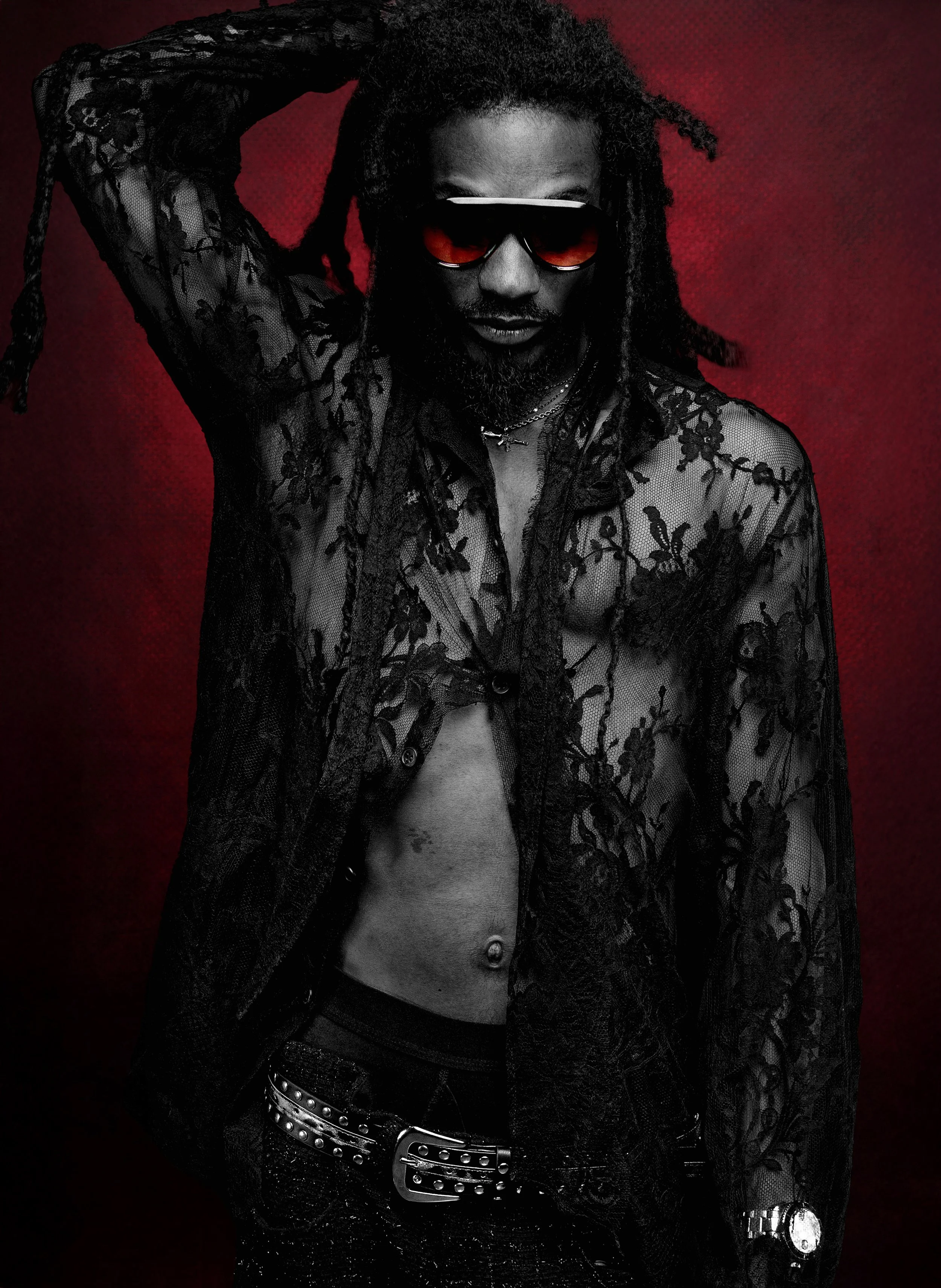 Portrait of a man wearing red sunglasses against a dark red background. SLICK