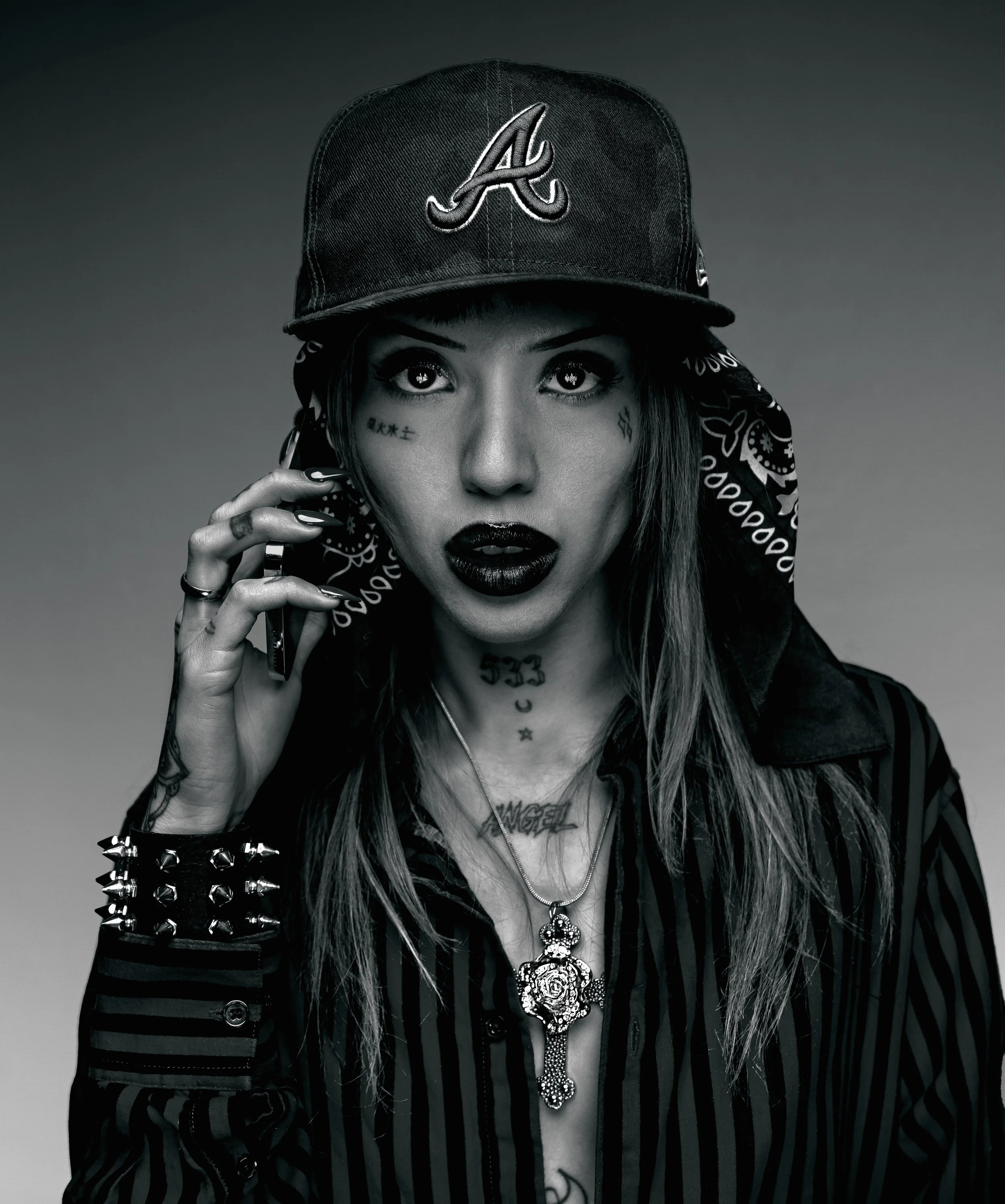 Black-and-white fashion portrait wearing a baseball cap and layered accessories. ANGELFACE