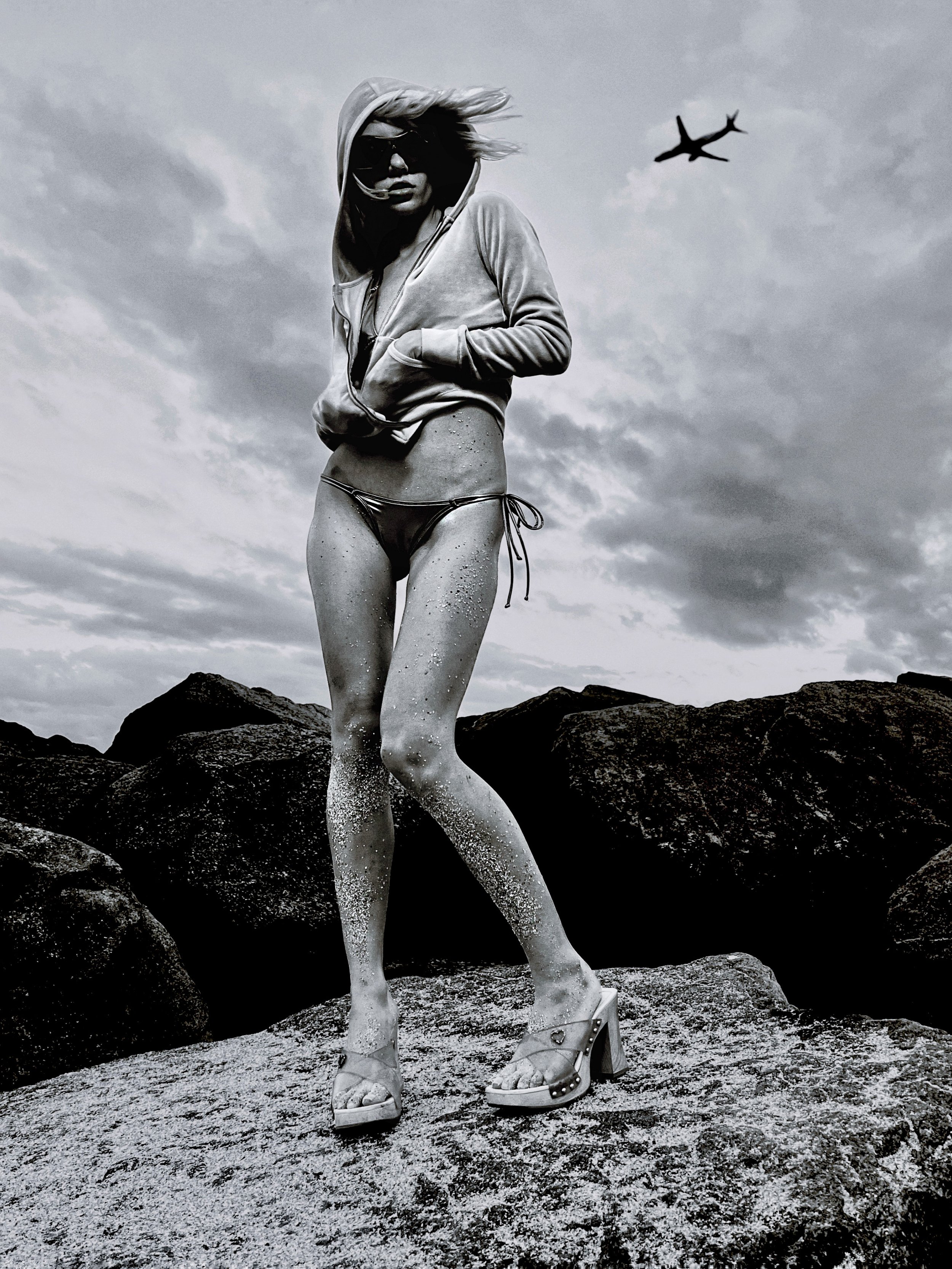 Black-and-white fashion portrait of a model standing outdoors on rocks. PARIS OSONA