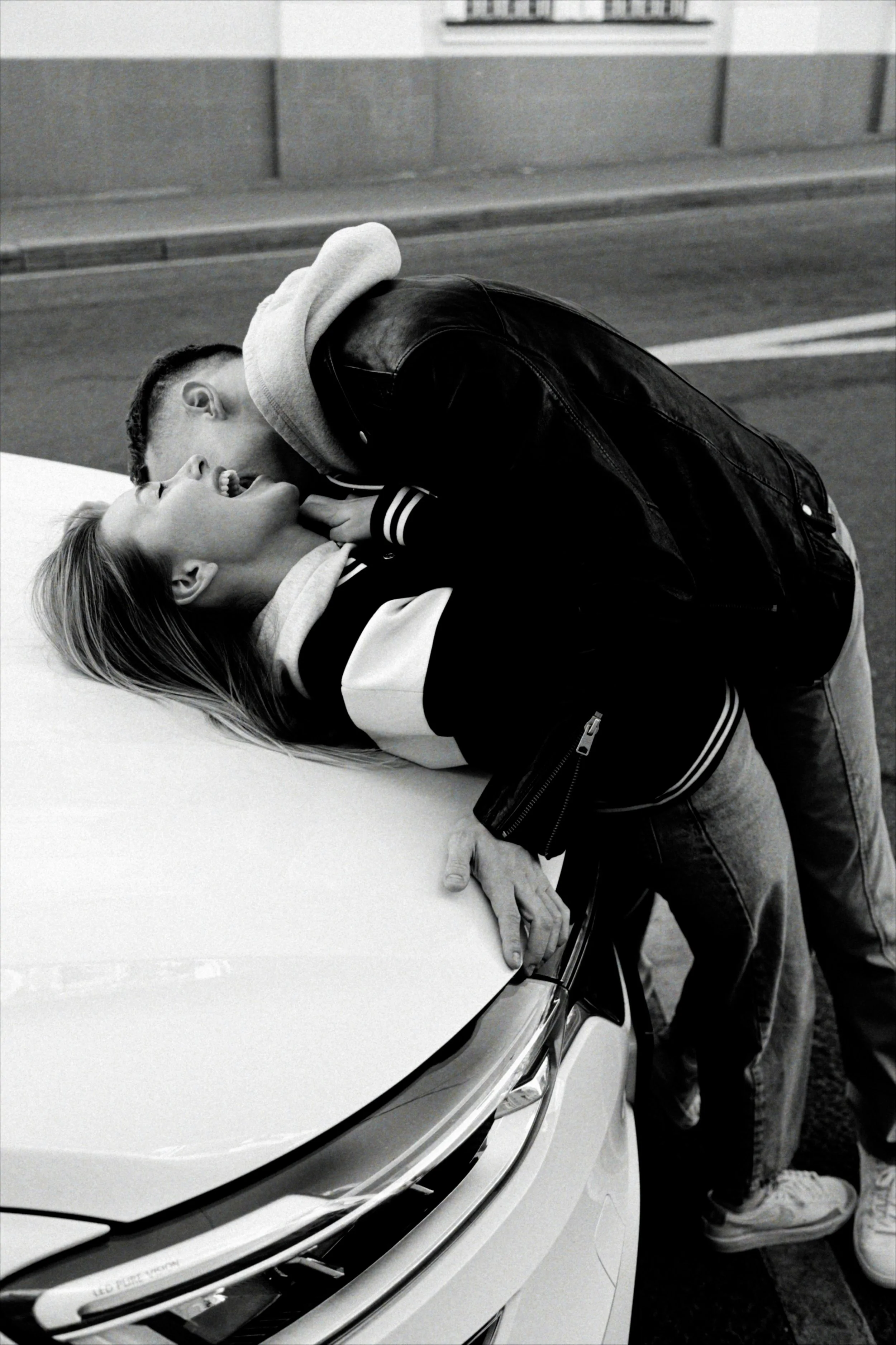 Black-and-white photo of a smiling couple embracing and kissing beside a piano.