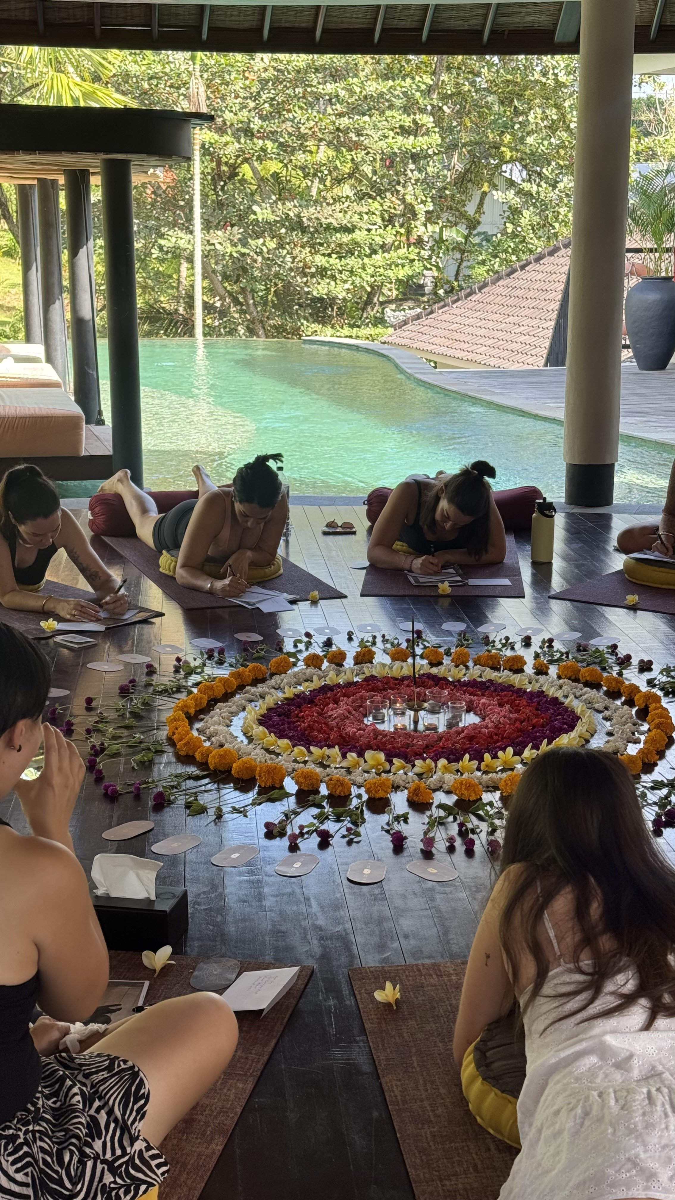 People practicing yoga beside a swimming pool with a large circular flower mandala and candles on the floor.