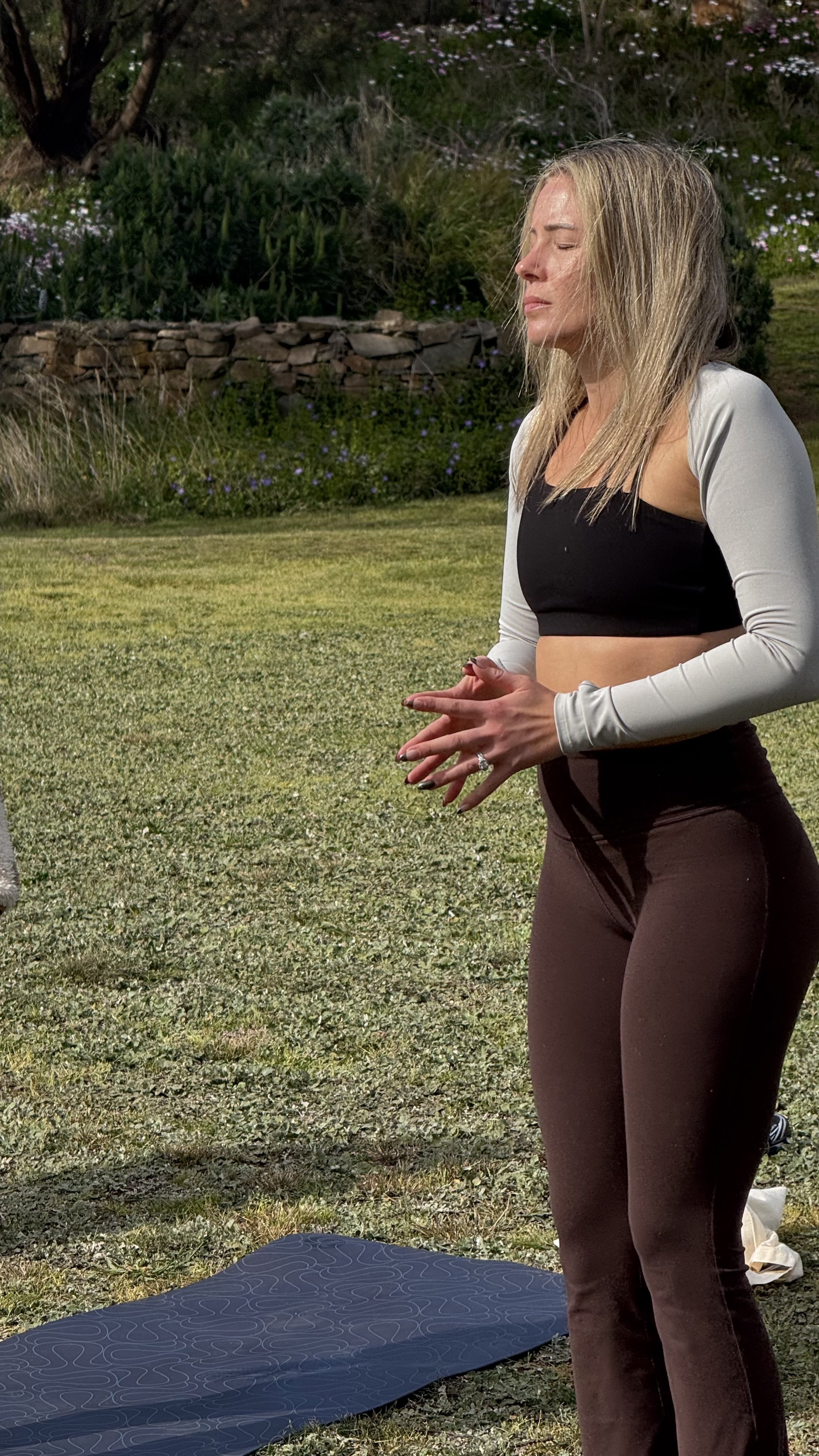 Woman practicing yoga outdoors on a mat in a flower-filled garden