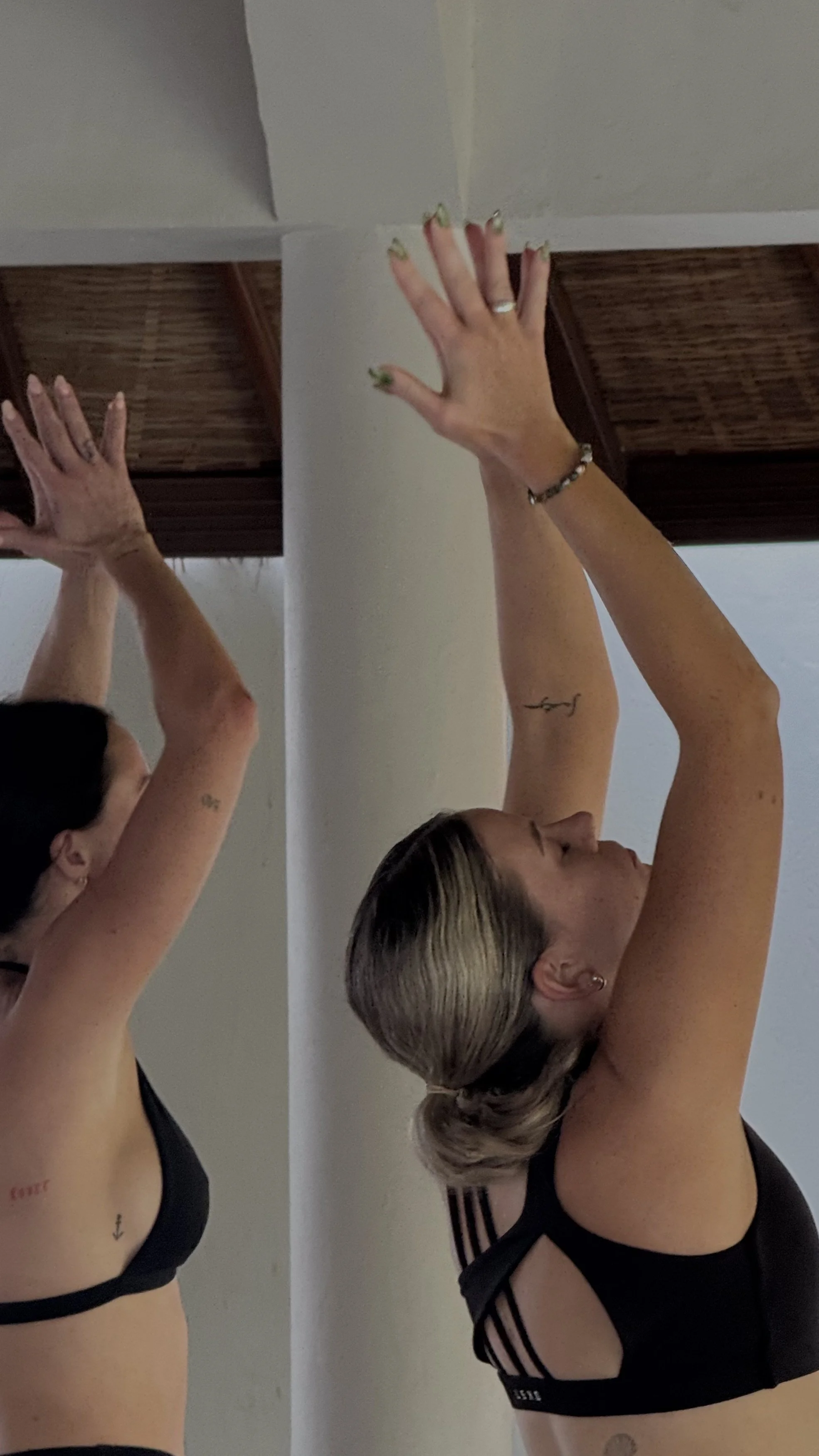 Woman in black workout clothing stretching with both hands against a wall beside a mirror.