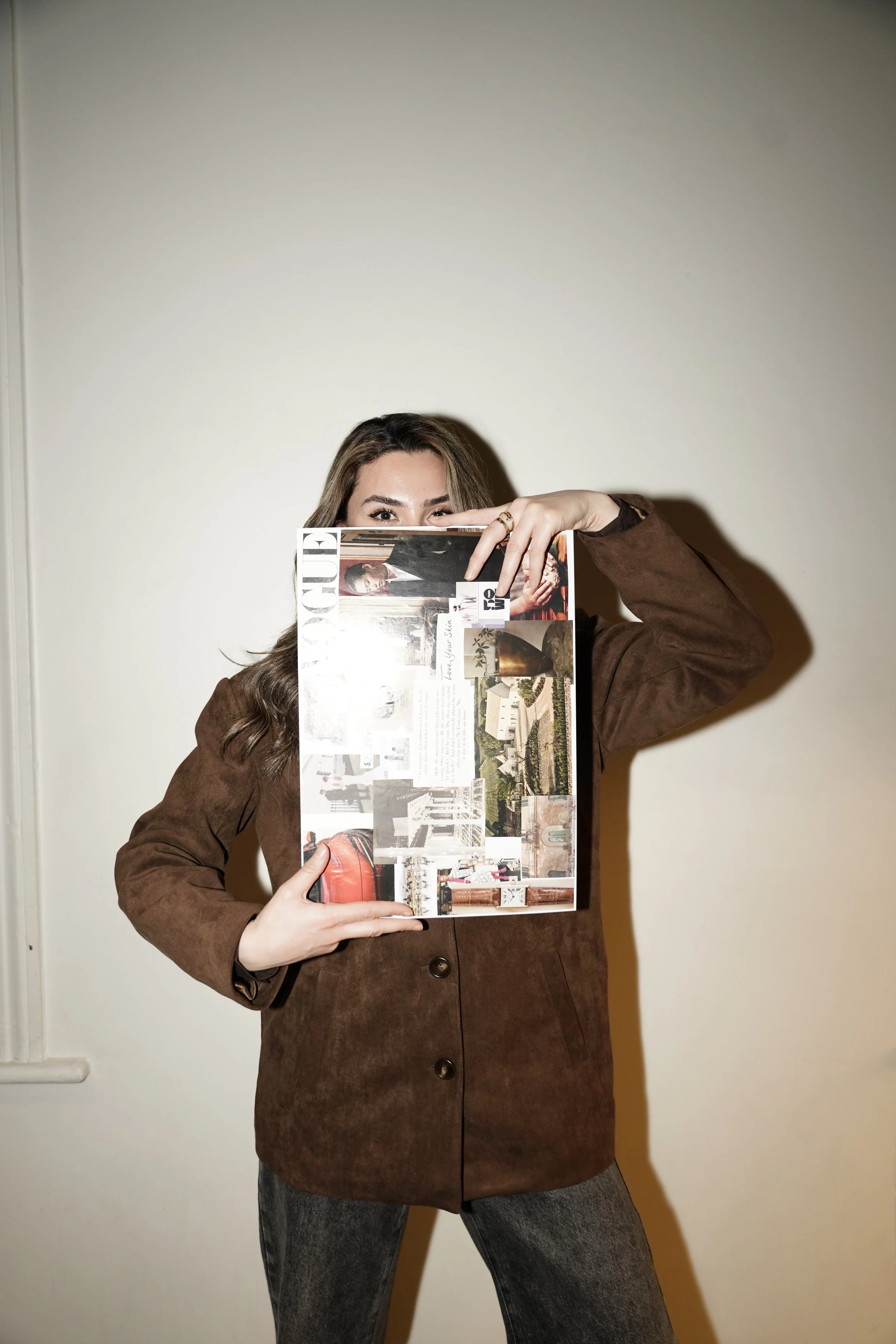 Woman in a brown jacket holding a large lifestyle magazine collage in front of her face