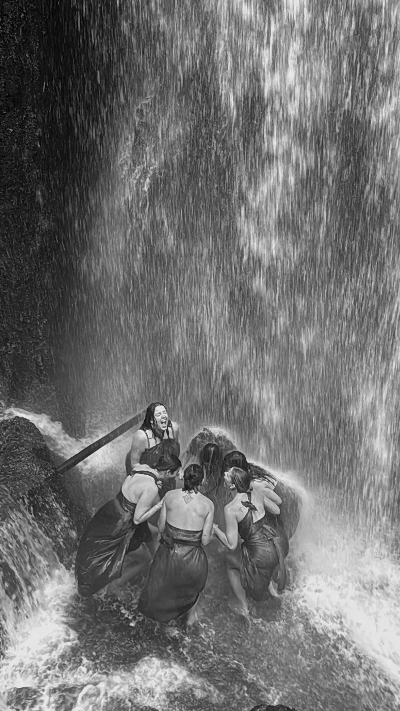 Group of people standing beneath a powerful waterfall in a traditional Balinese purification ceremony