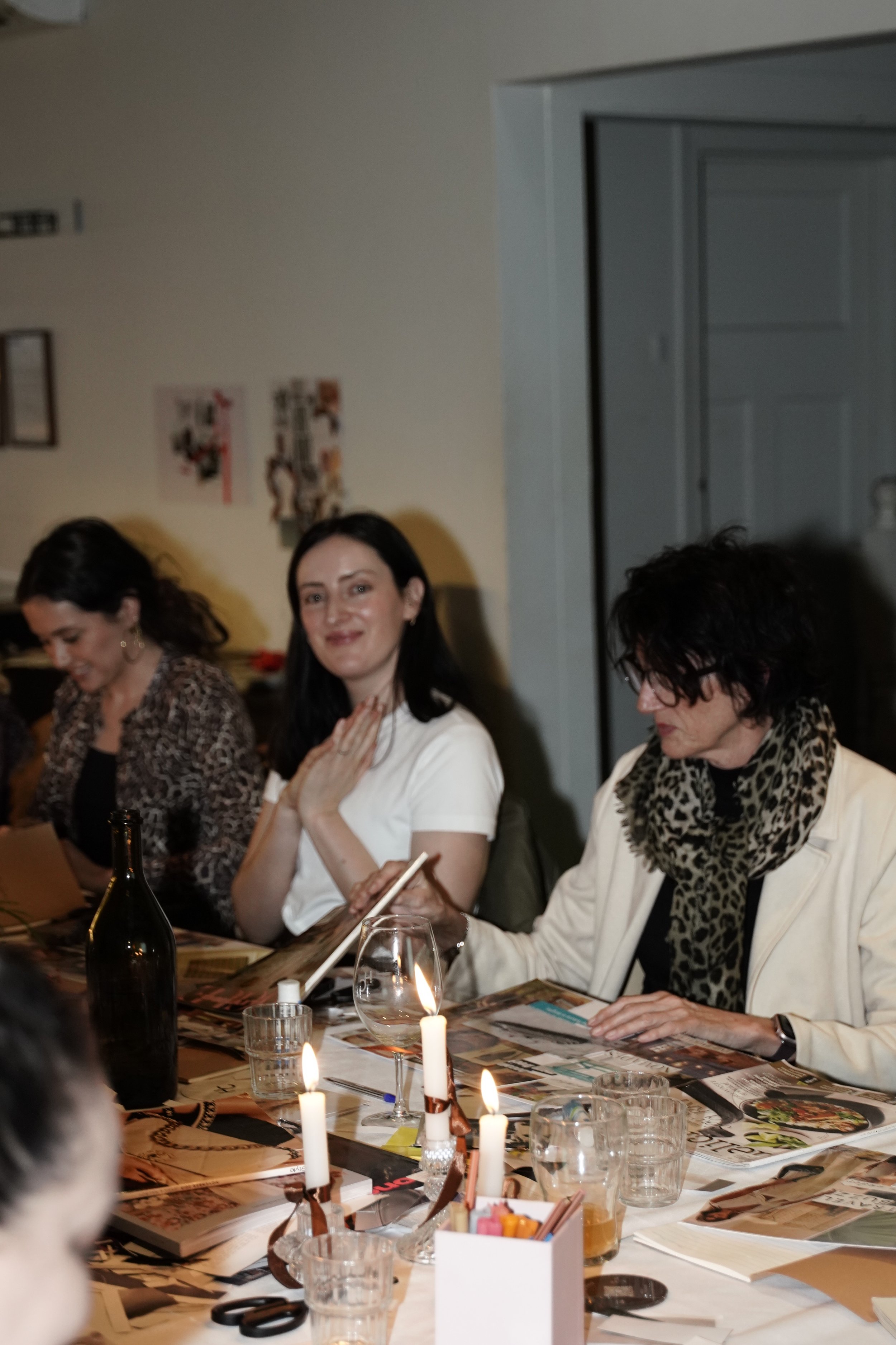 People gathered around a candlelit restaurant table with wine, menus, and glasses.