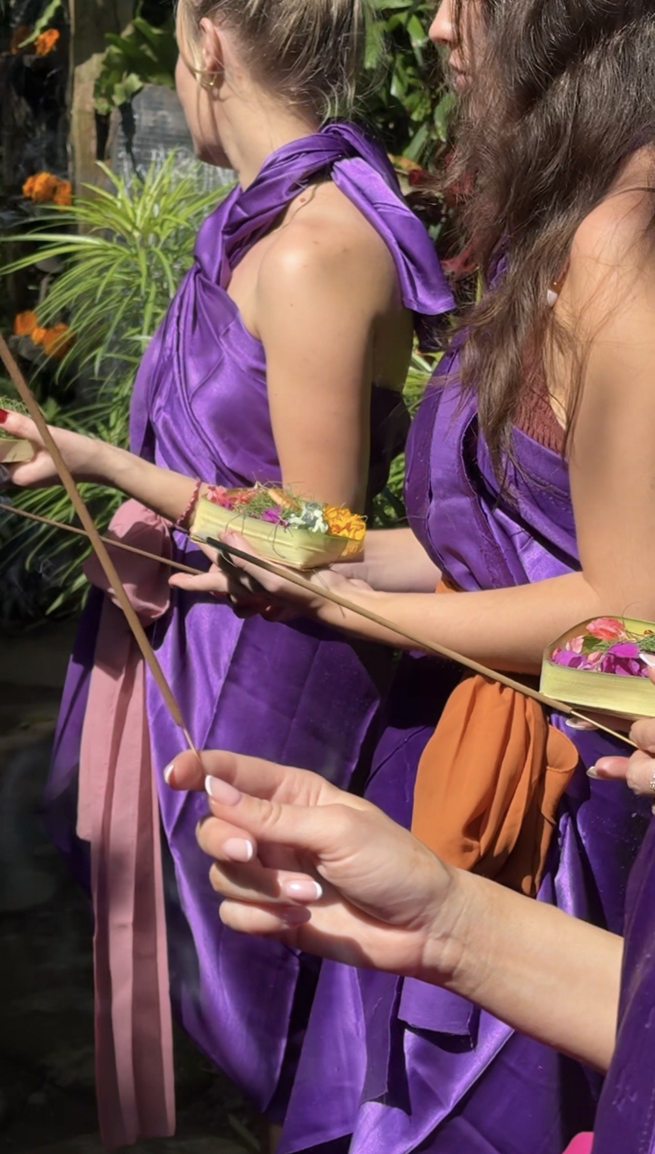 People in purple clothing holding colorful floral offerings outdoors