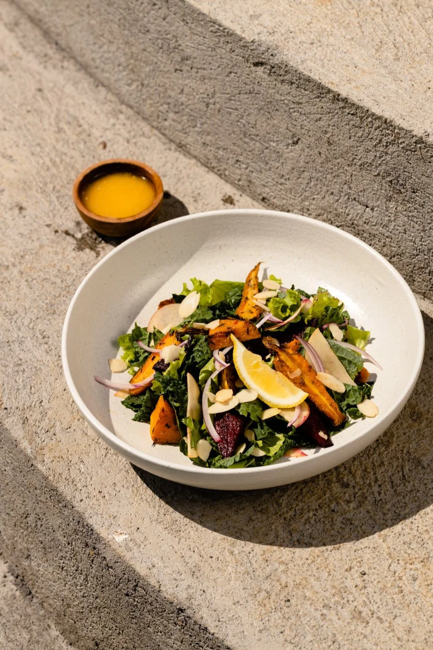 Roasted carrot and beet kale salad with almonds, red onion, lemon wedge, and yellow dressing