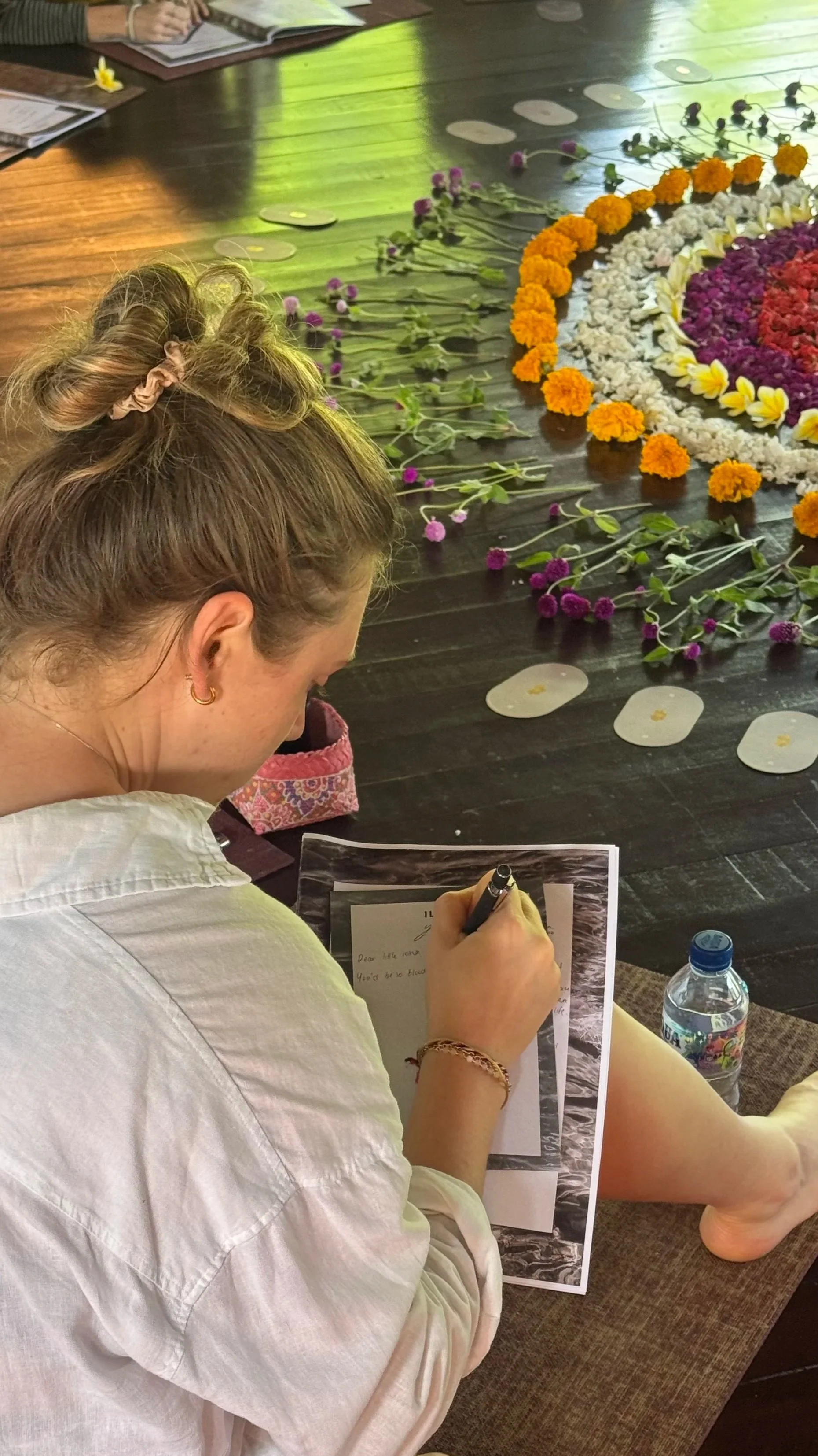 Woman writing beside a colorful floral arrangement on a dark table