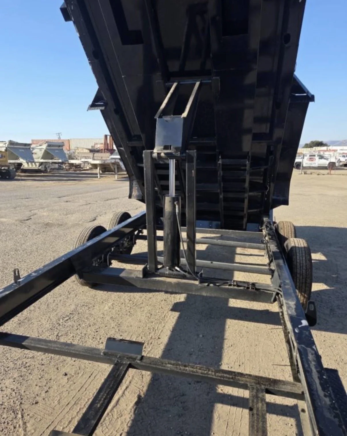A black hydraulic dump trailer with its bed tilted upwards, revealing the interior mechanism for dumping material