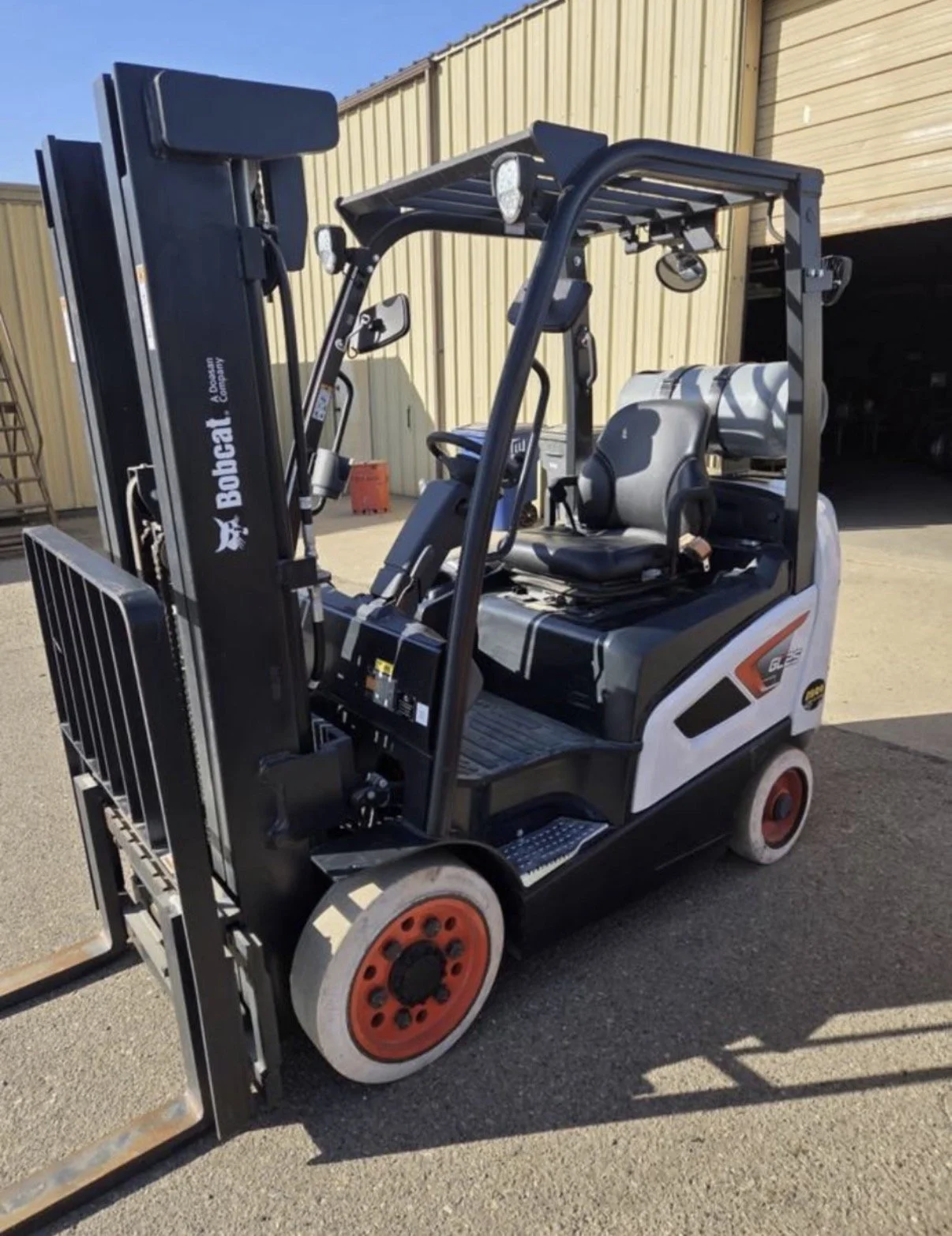 Electric forklift with black and white body and red wheels, parked outdoors next to a yellow building with a garage door.