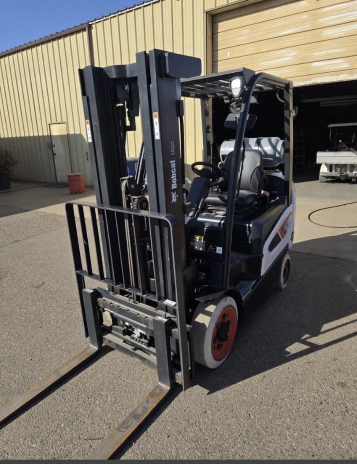 A Bobcat electric forklift on an outdoor concrete surface in front of a yellow metal building with a large open garage door.