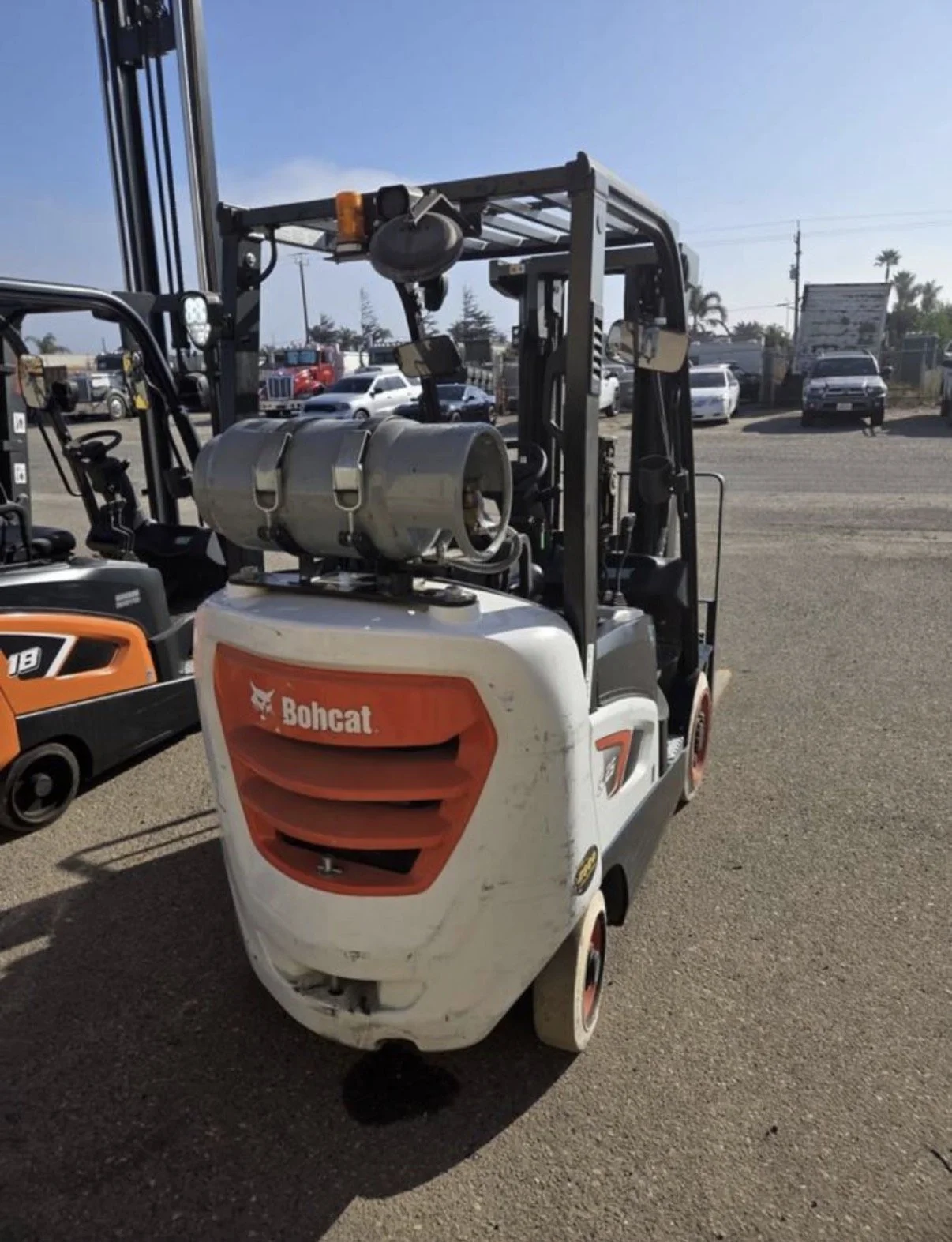 A white forklift with a propane tank mounted on the front, parked outdoors in a lot with other vehicles. The forklift has a red grille with the brand name 'Bohcat'.