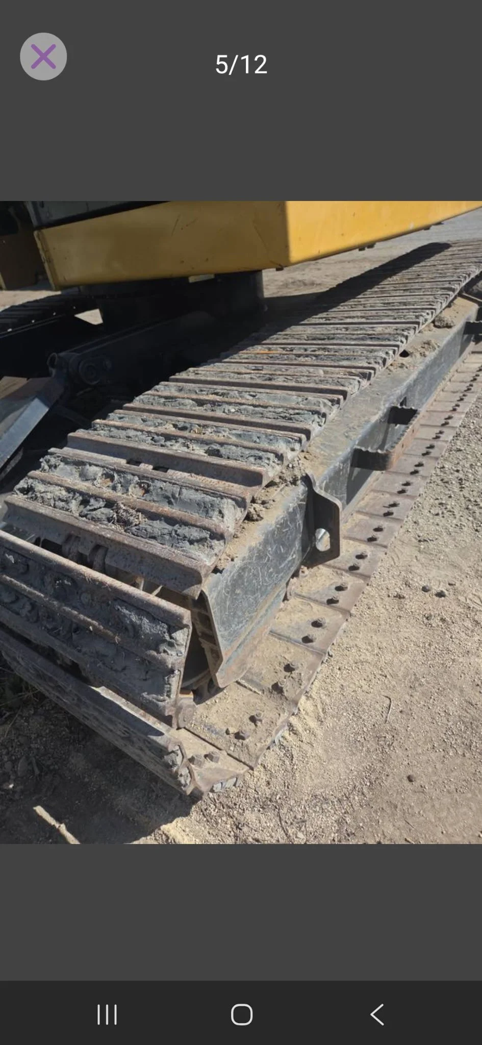 Close-up of a dirt-covered construction vehicle track on a sandy surface.