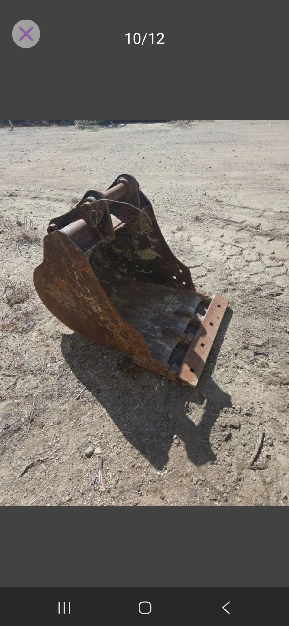 Rusty excavator bucket lying on dry, cracked dirt ground in a barren landscape.