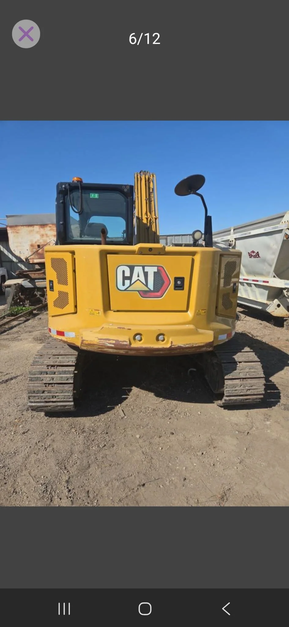 Yellow CAT excavator parked on dirt ground with tracks and a black cab under a clear blue sky.