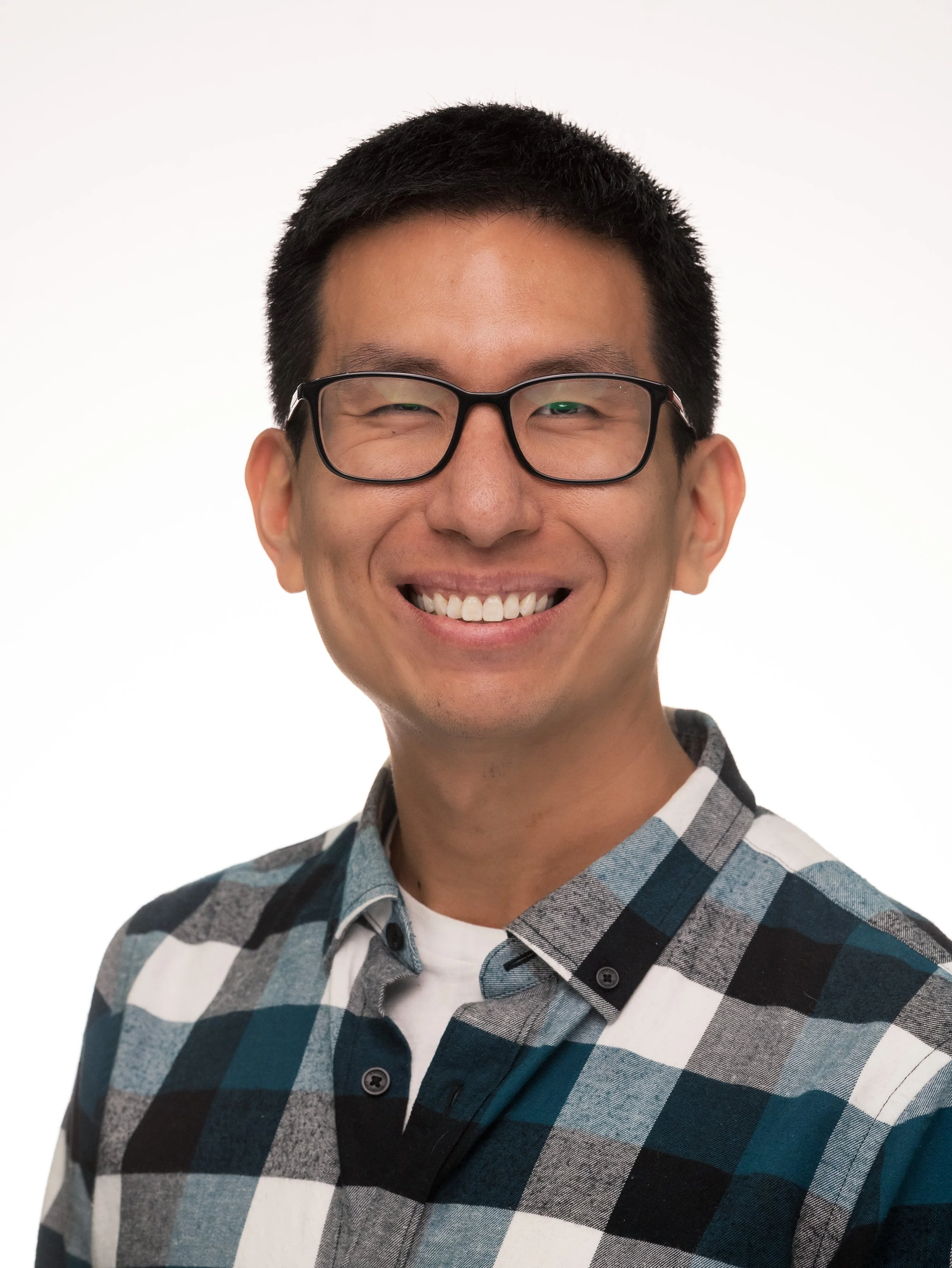 A smiling man with short black hair, glasses, and a checkered shirt, against a plain white background.