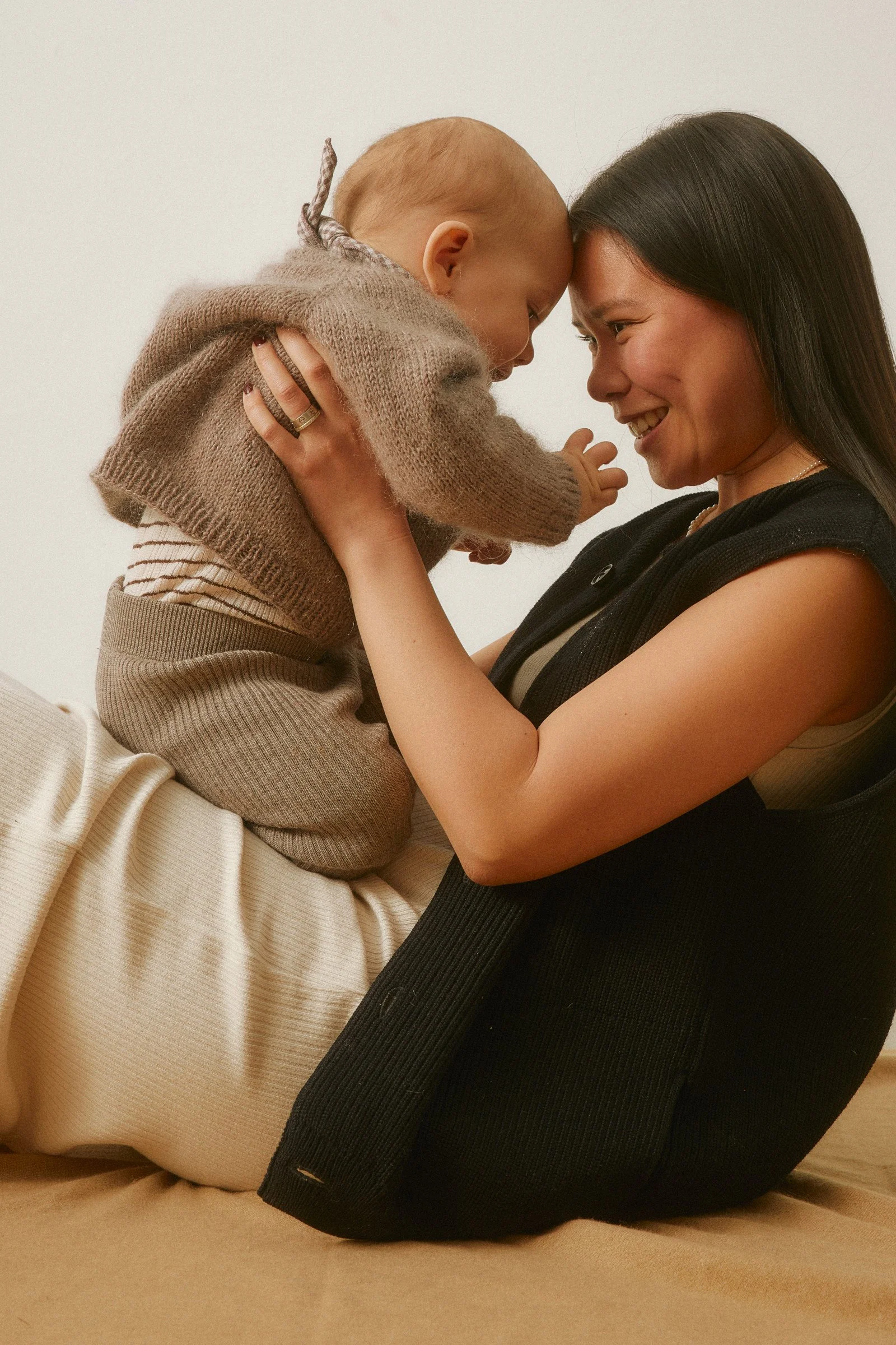 A woman and a child with their foreheads touching and smiling, holding each other affectionately indoors.