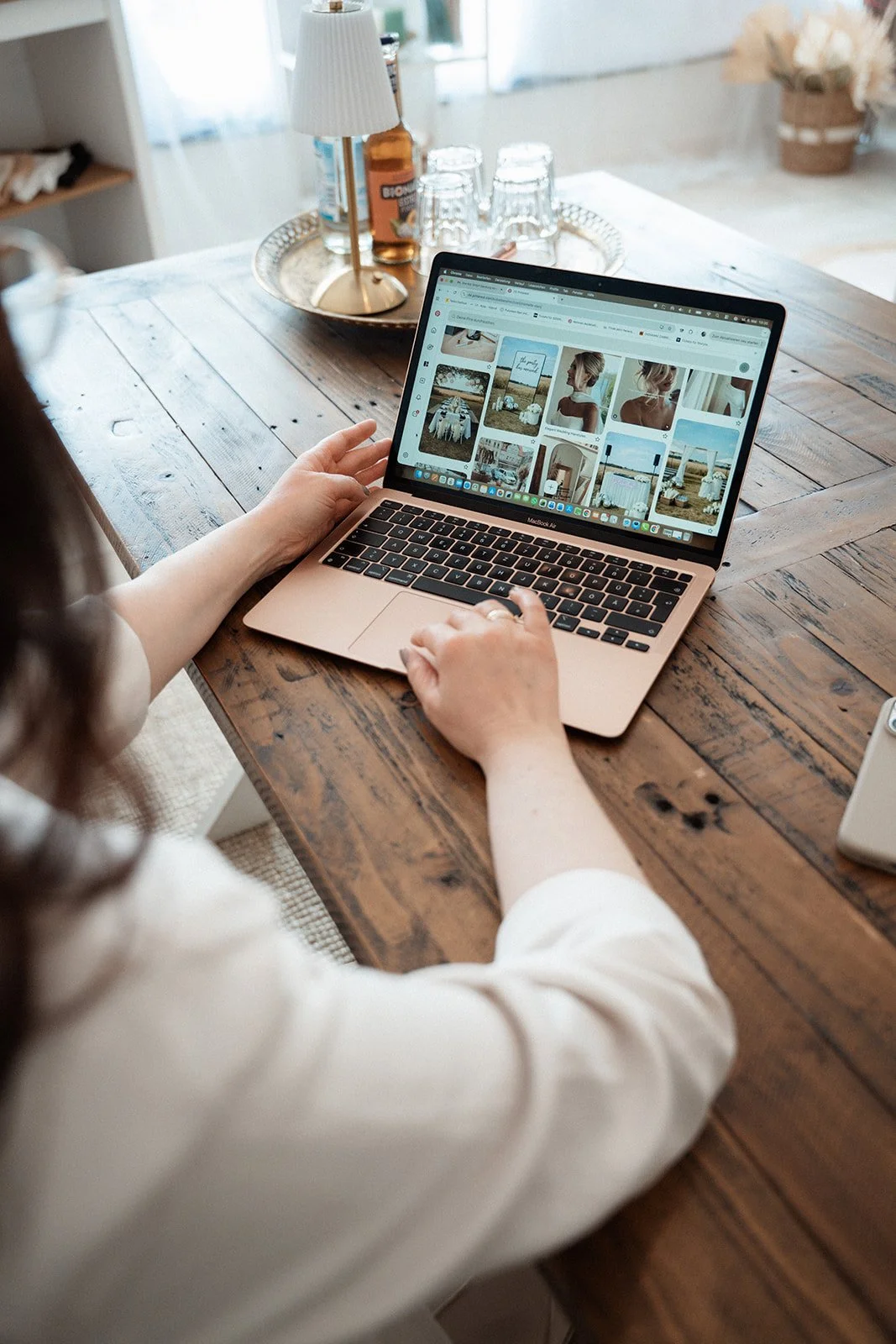 Person, die an einem Laptop sitzt und auf eine Webseite mit Fotos schaut, auf einem Holztisch.
