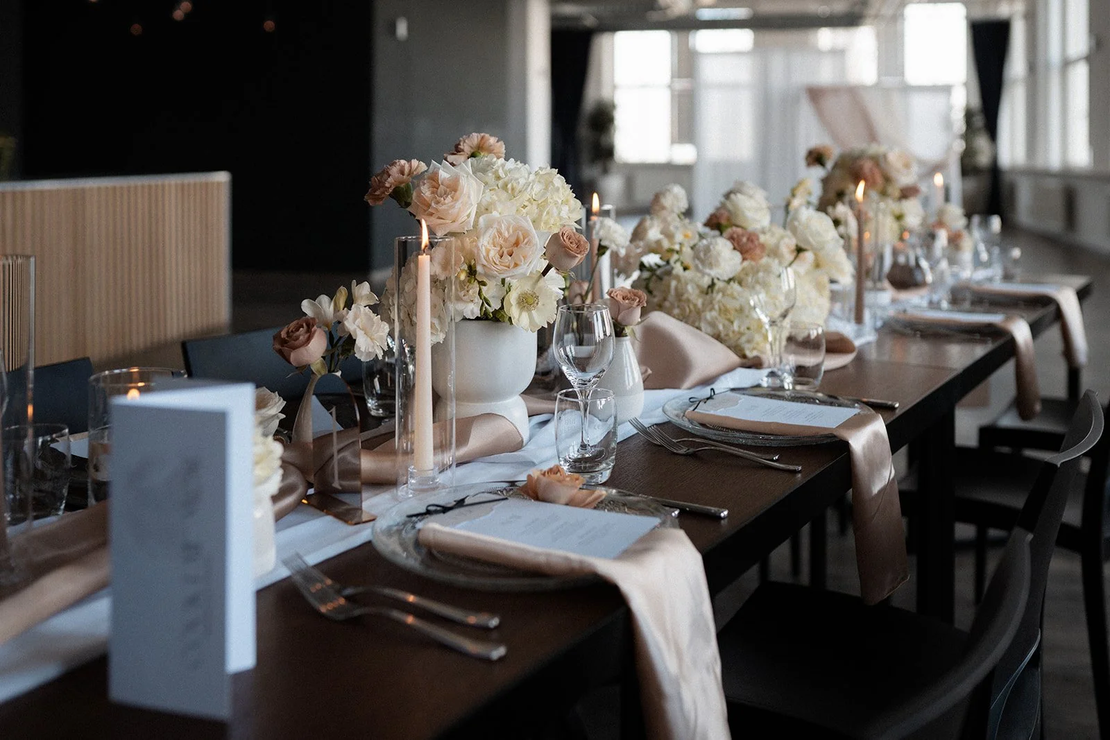 Ein elegant gedeckter Tisch mit weißen Blumenarrangements, Kerzen und formeller Tischware in einem gut beleuchteten Raum.