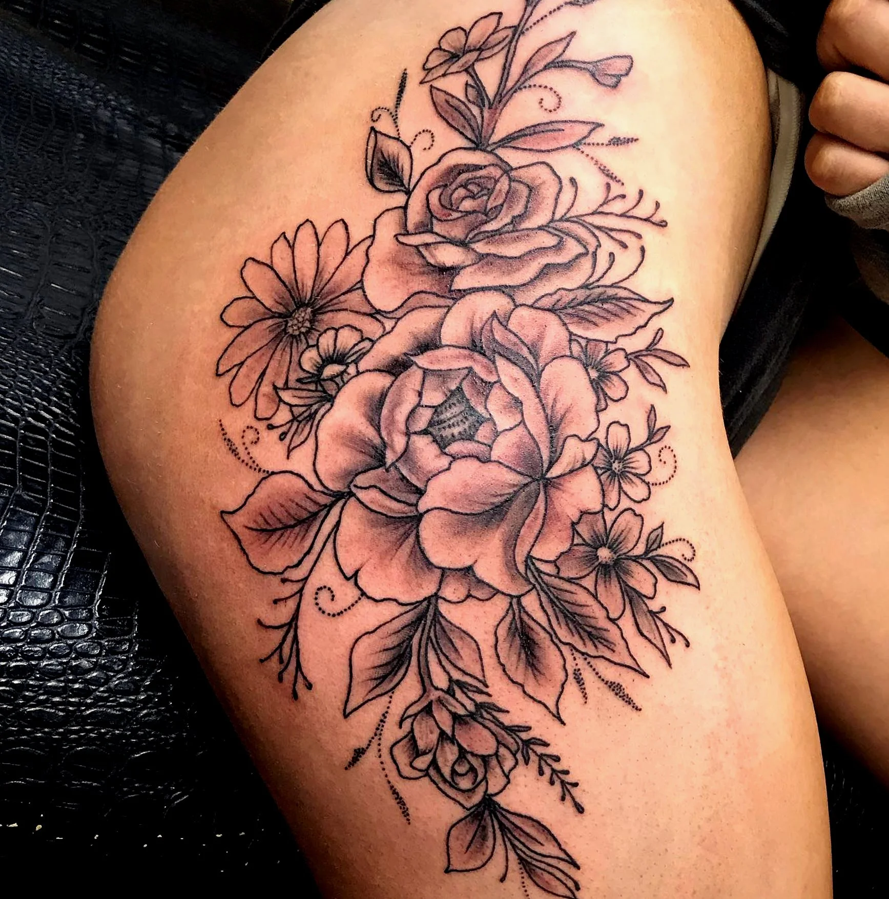 Black outline floral tattoo featuring roses, daisies, and leaves on a person's arm.