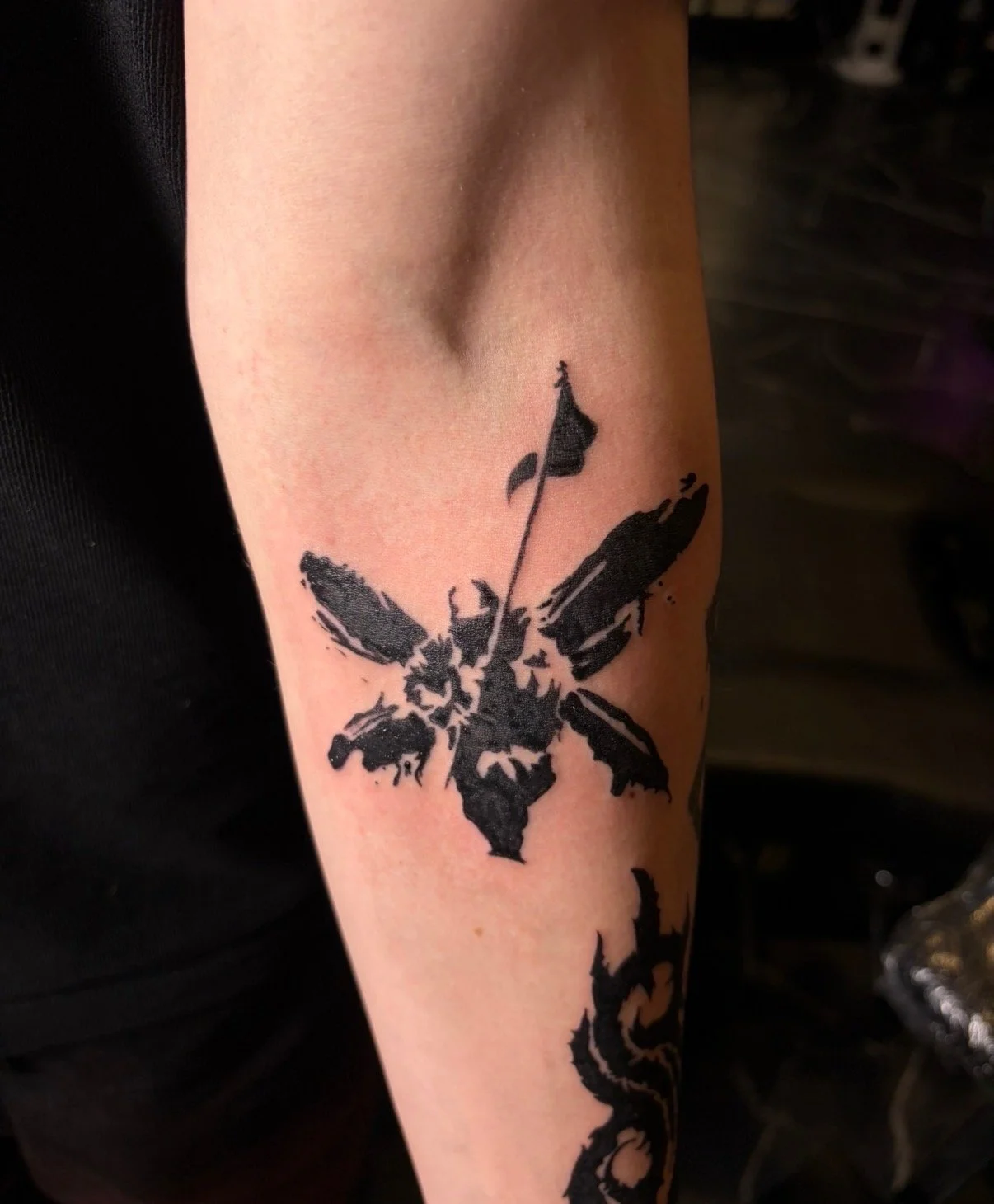 Tattoo of a black butterfly with incomplete and splattered wing details on a person's upper arm.