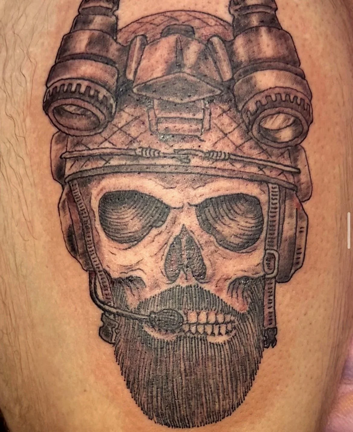 Tattoo of a human skull wearing military helmet with goggles and headphones, and a beard.