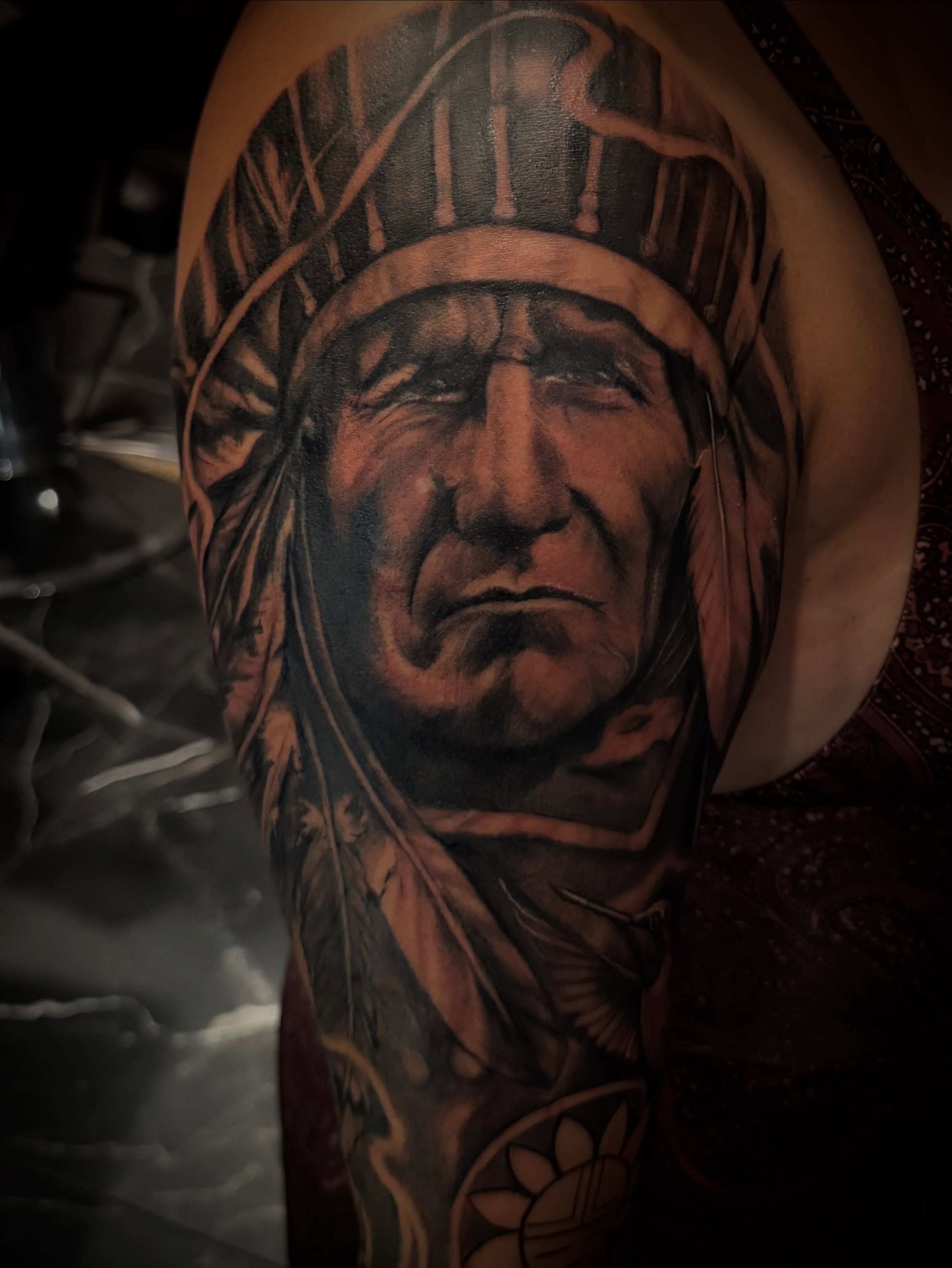 Tattoo of a Native American chief wearing a feathered headdress on a person's upper arm.