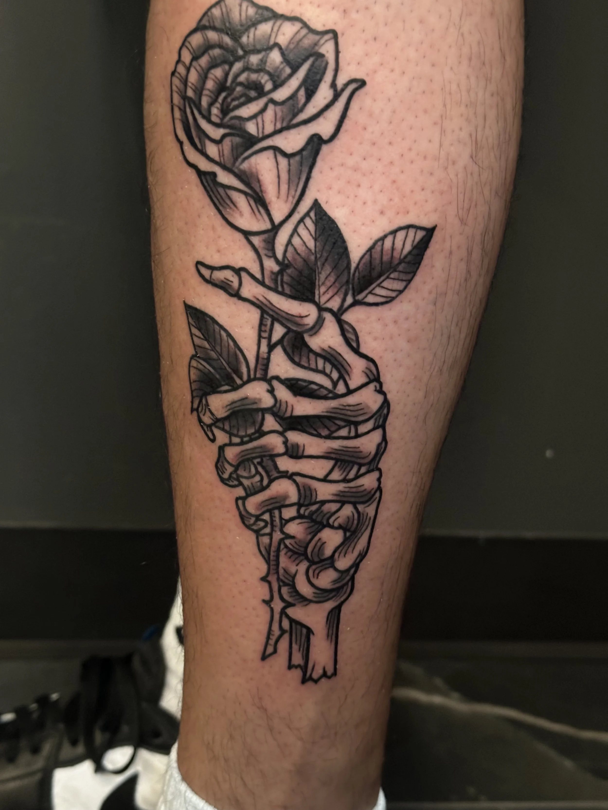 Black outline tattoo of a rose with a hand gripping the stem on a person's forearm.
