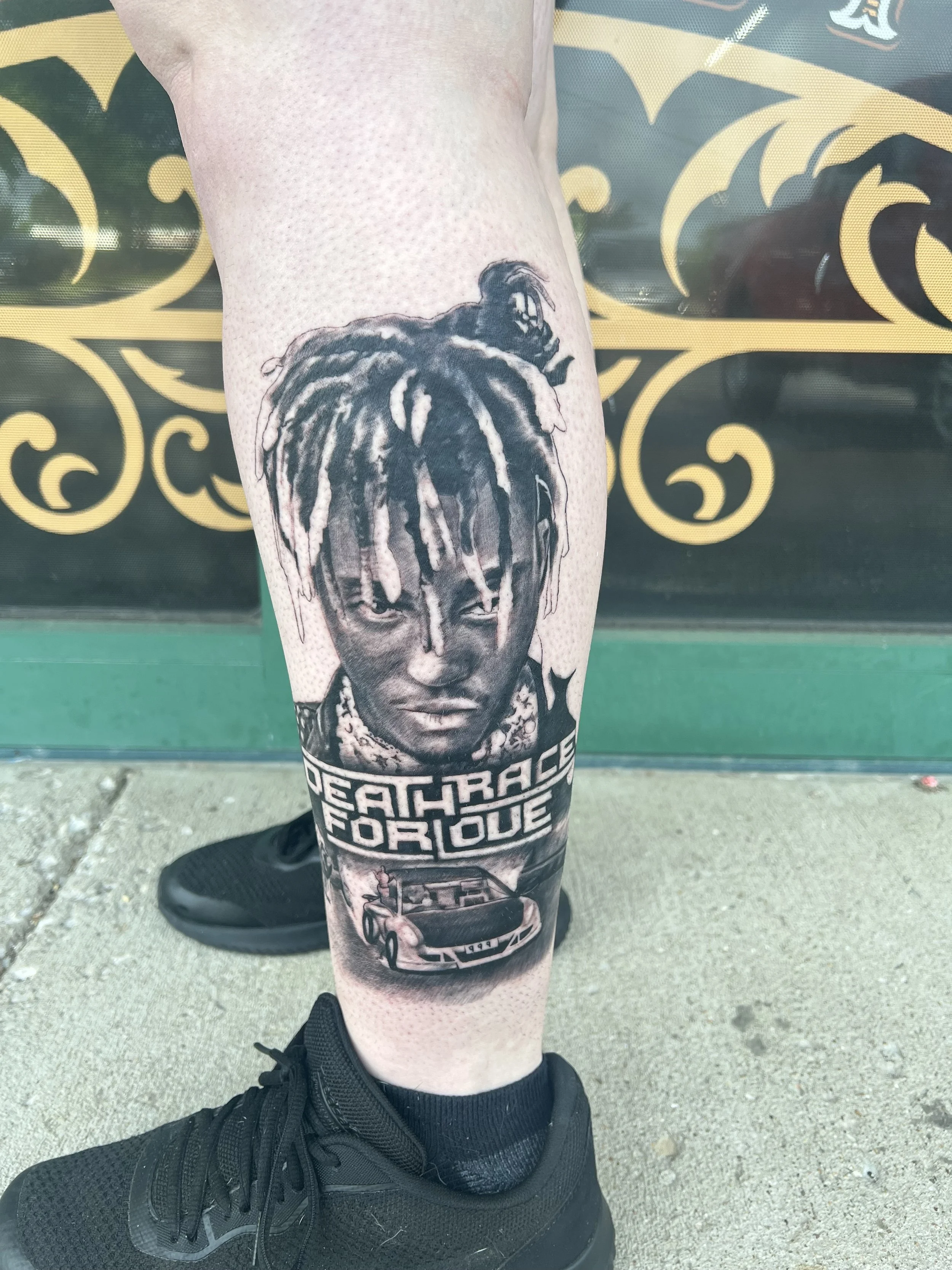 Tattoo of a woman's face with dreadlocks and a car with the caption 'LEACH RACER FOR LIFE' on a person's lower leg with black athletic shoes.
