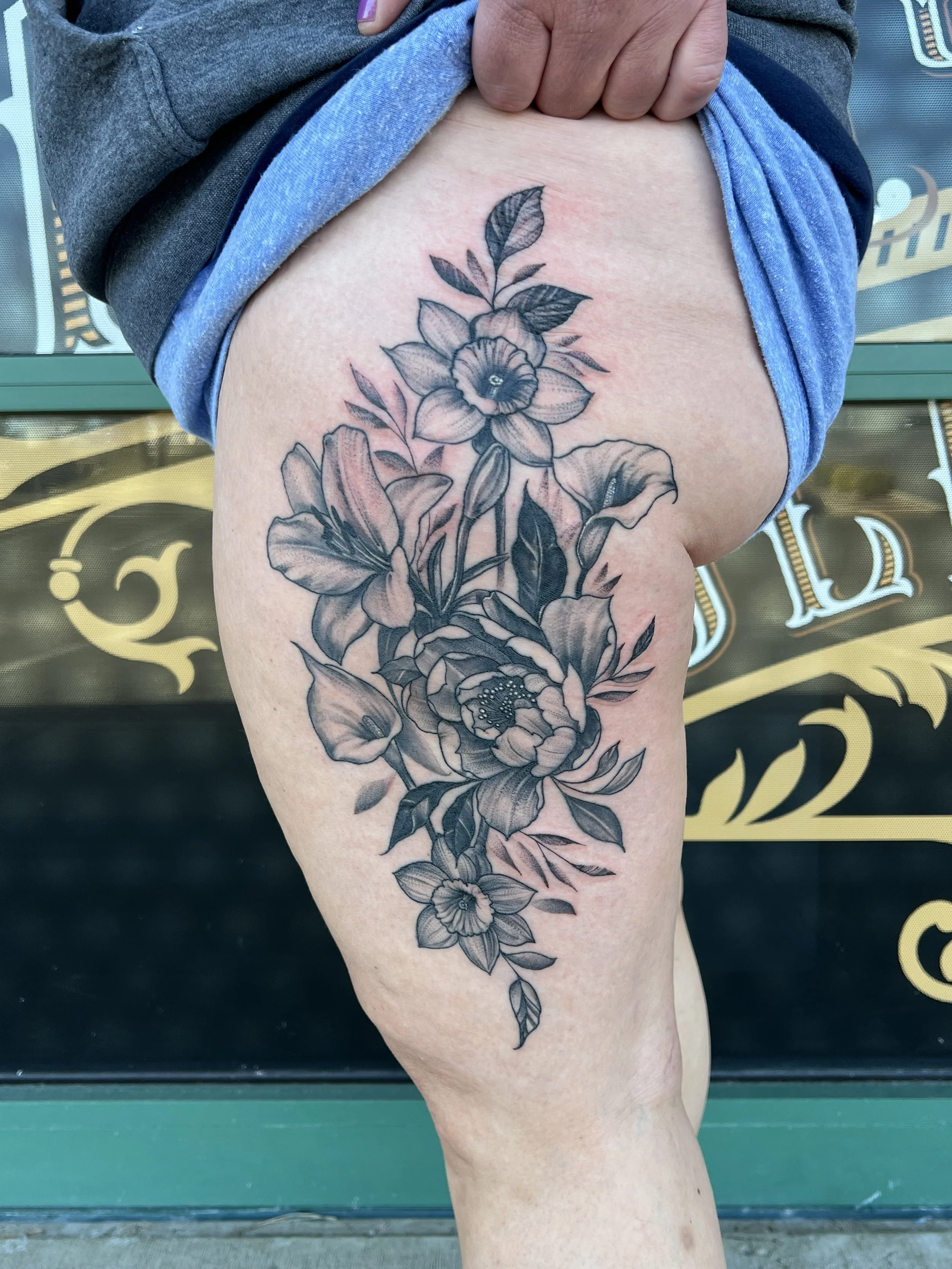 A large floral tattoo on a person's upper thigh, depicting multiple flowers and leaves in black and gray ink.